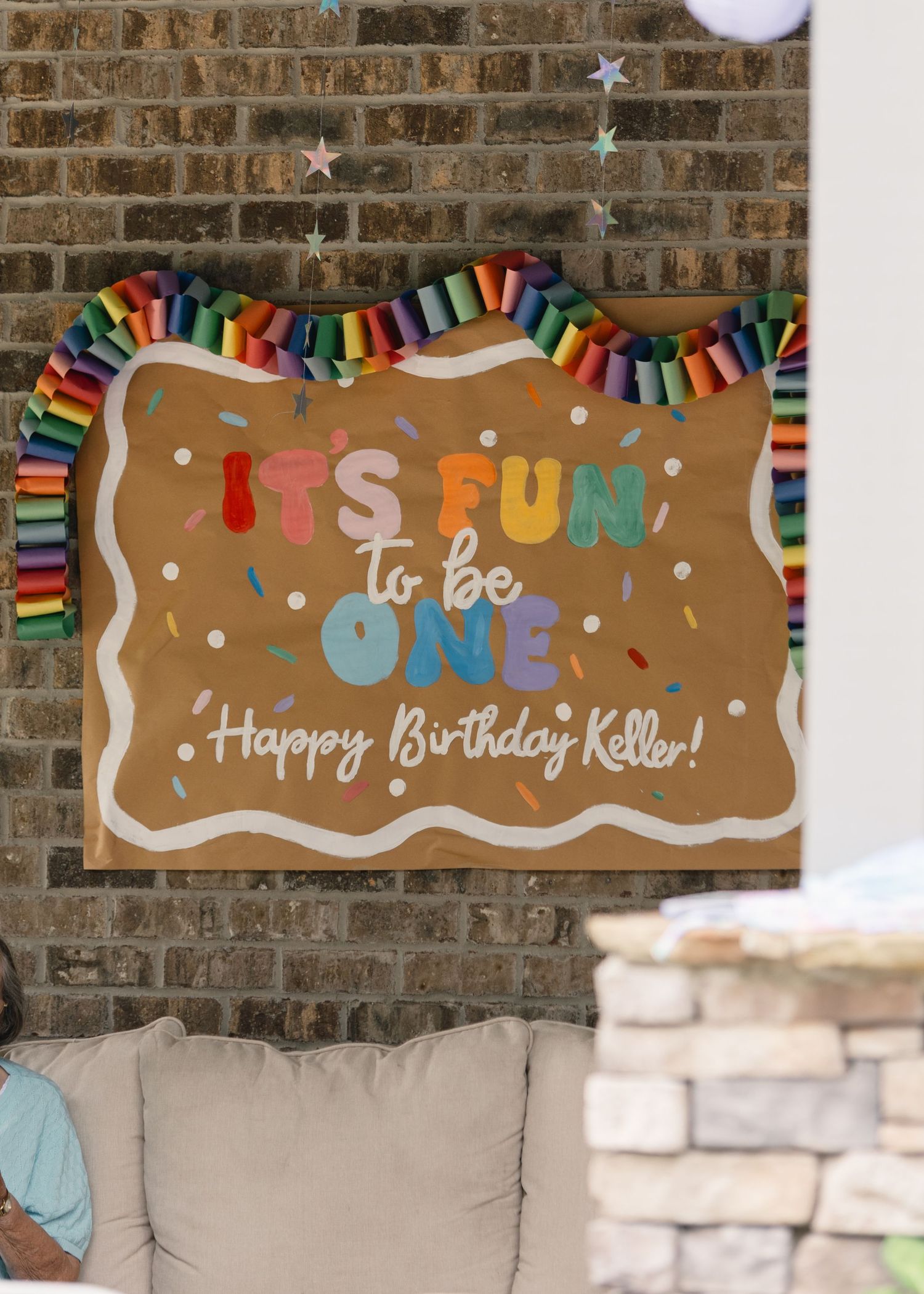 Colorful birthday sign reading Its Fun to Be One Happy Birthday Keller mounted on a brick wall.