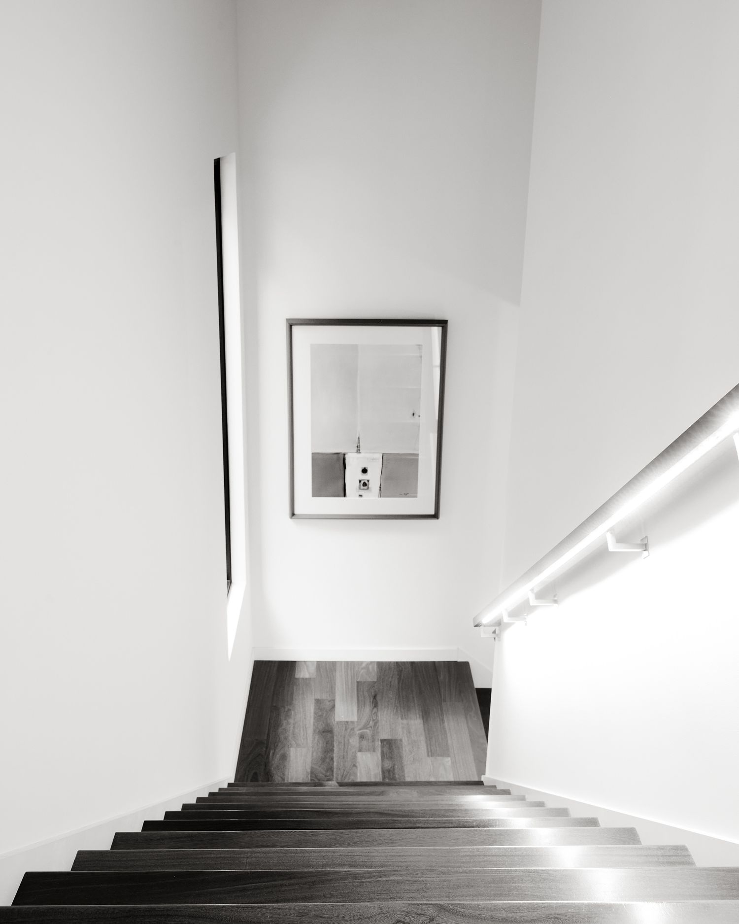 Minimalist black and white staircase with wooden steps, white walls, and a framed artwork hanging in the landing area.