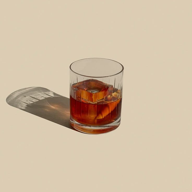 Whiskey on the rocks in crystal glass casting shadow on beige background.