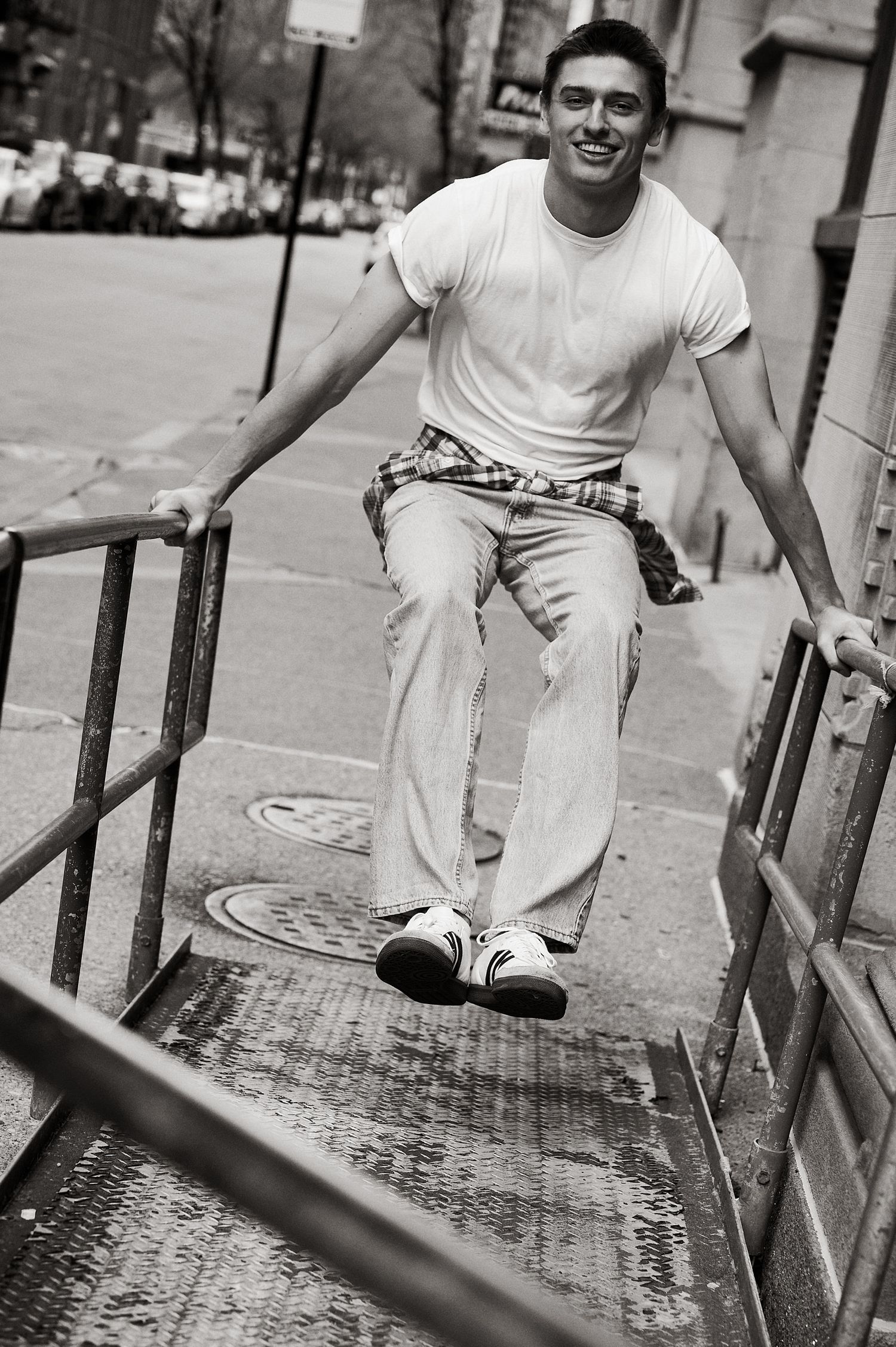 Young man in white t-shirt and jeans descending urban stairs, smiling, with flannel tied around waist.