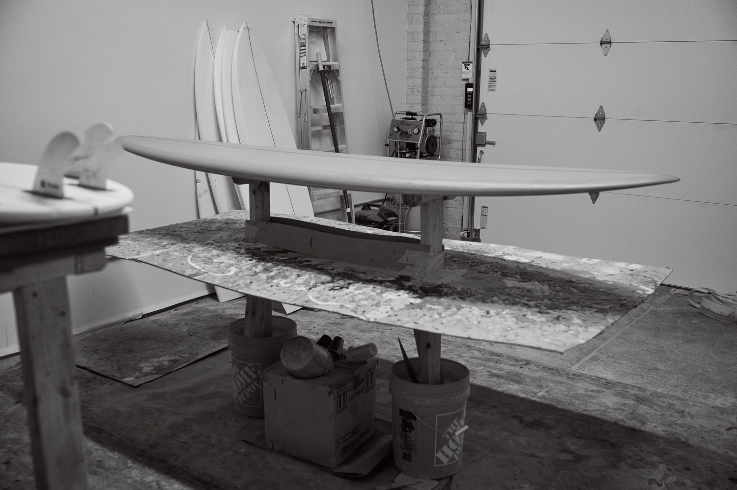Finished surfboard on workbench in shaping bay, black and white photography.
