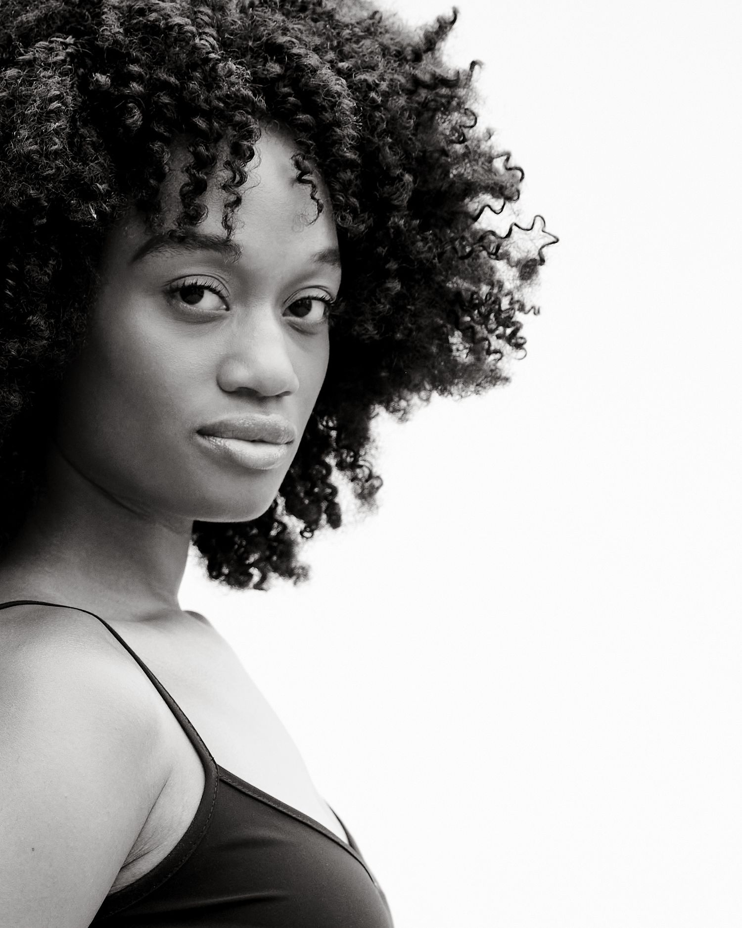 Black and white portrait of a young woman with voluminous natural curly hair wearing a black top.