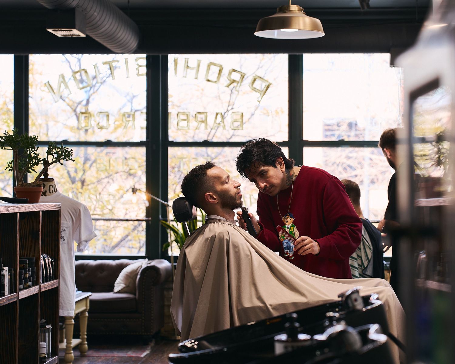 Barber giving a close shave to a client at Prohibition Barber shop with city views.