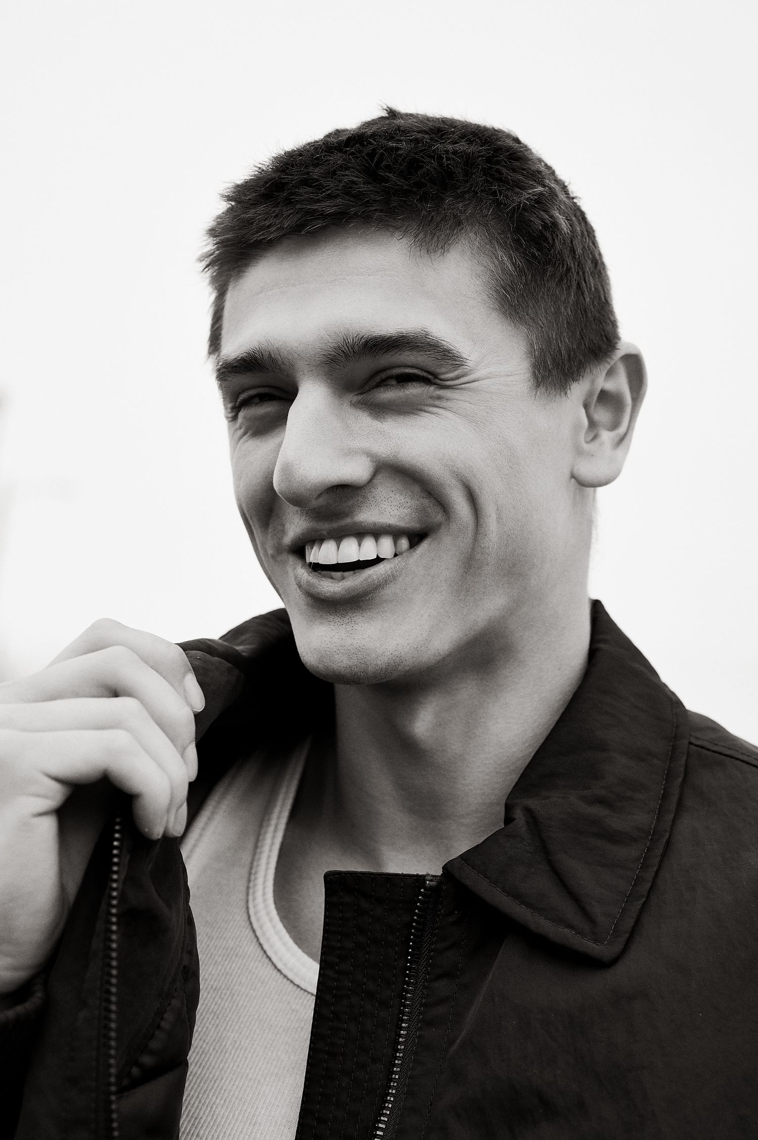 Black and white portrait of a smiling young man in a jacket against a light background.