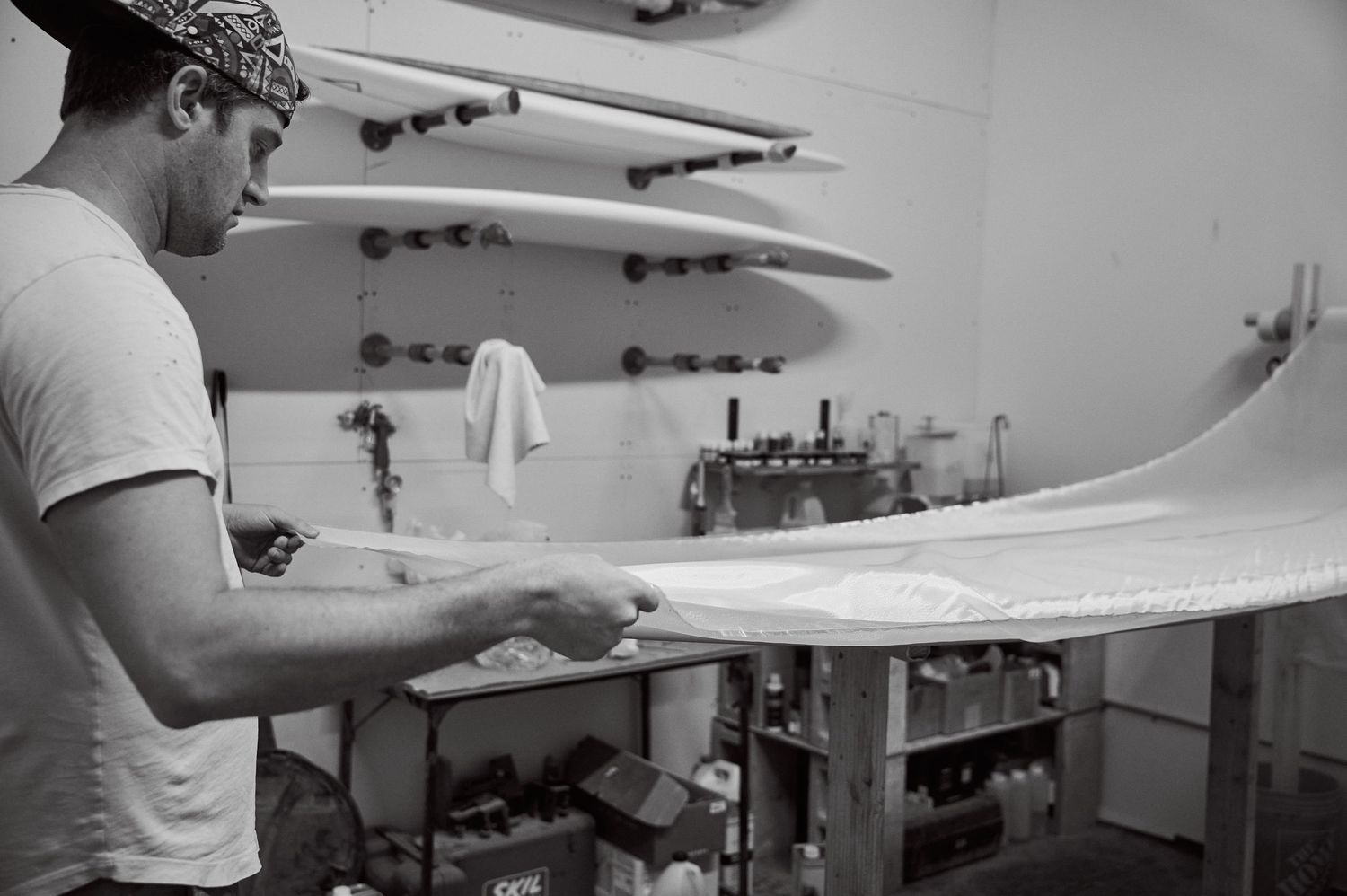 A craftsman carefully sands a surfboard in a well-equipped shaping bay workshop.