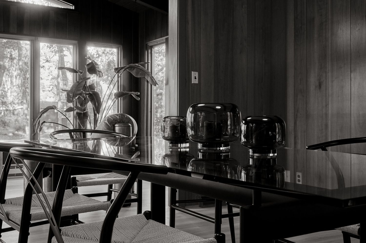 Black and white photo of a dining room with glass pitchers on a table and a bicycle visible by large windows.