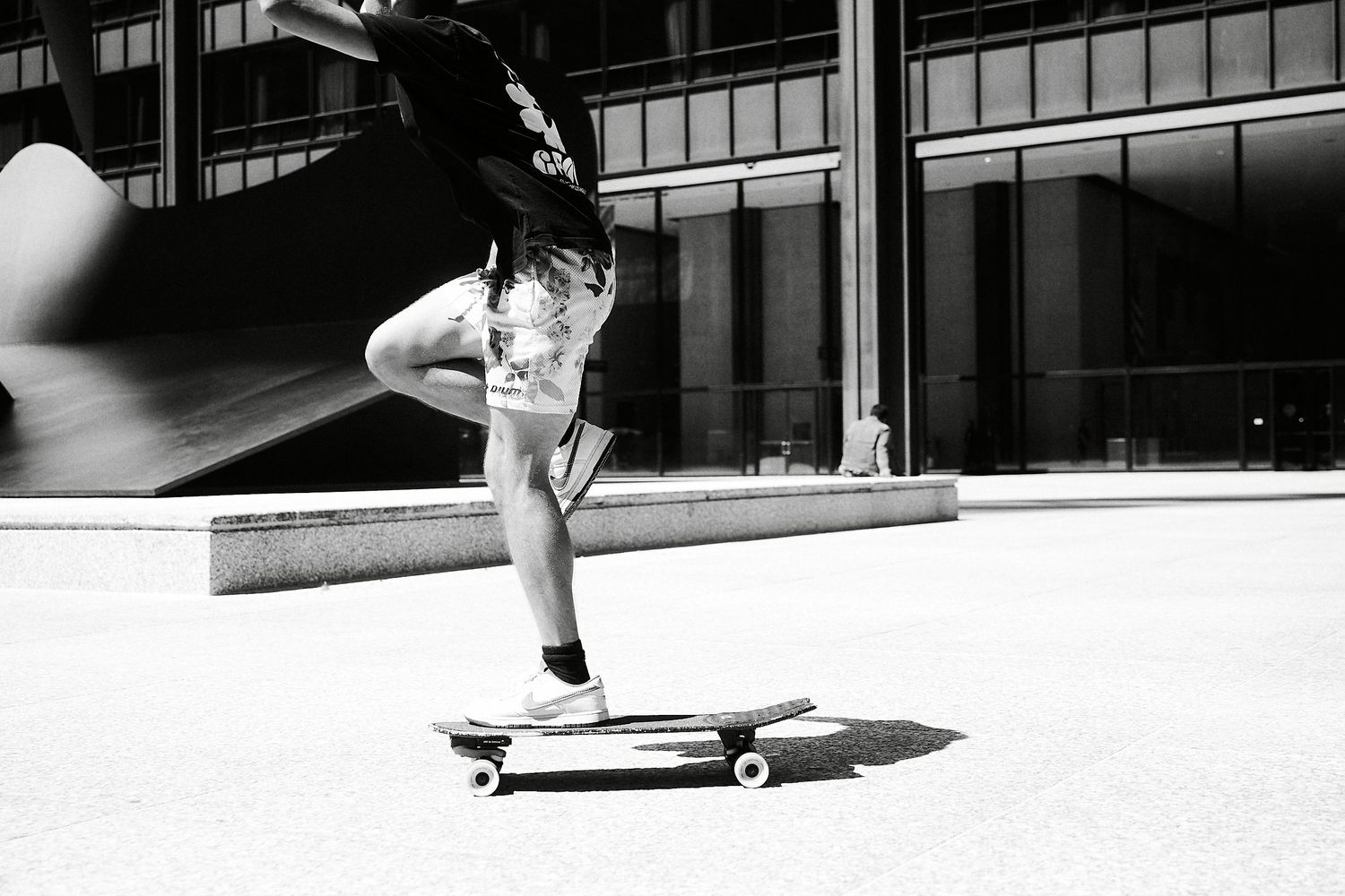 Black and white shot of a skateboarder performing a trick on a longboard in an urban plaza.