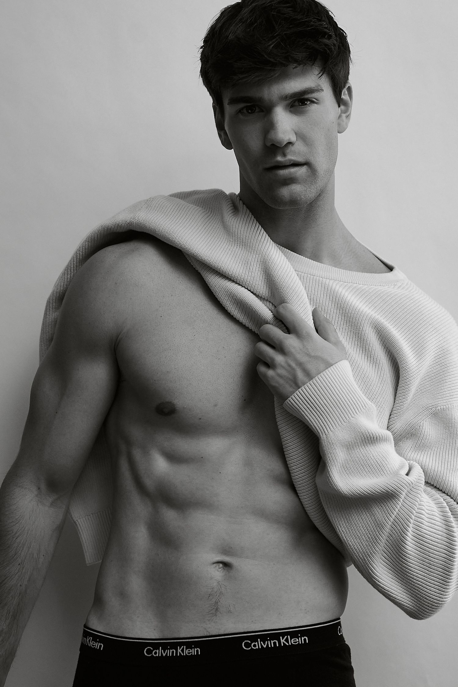 Black and white photo of a fit man in Calvin Klein underwear lifting his sweater to reveal toned abs.