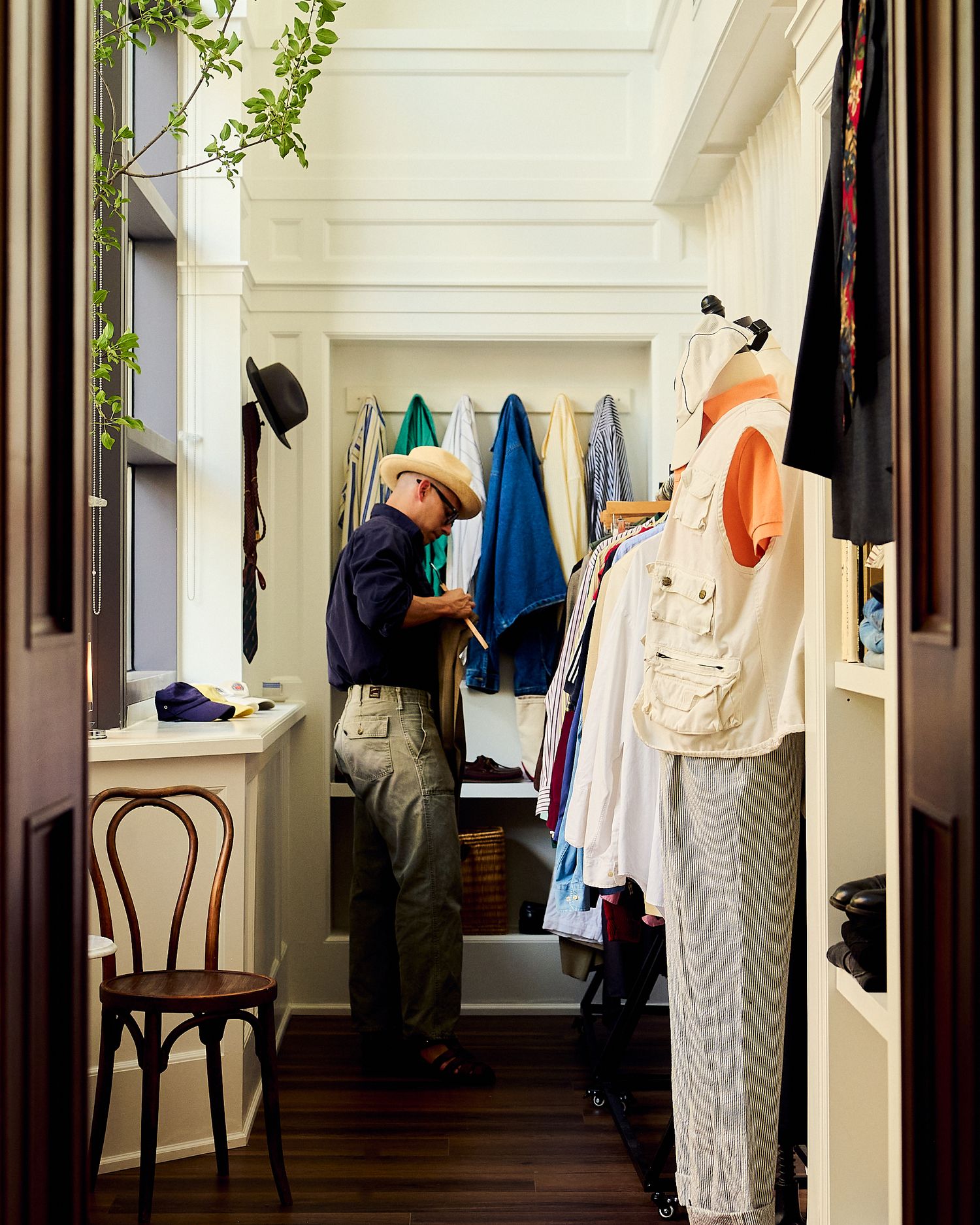 Man in straw hat browsing colorful hanging clothes in a well-organized walk-in closet.