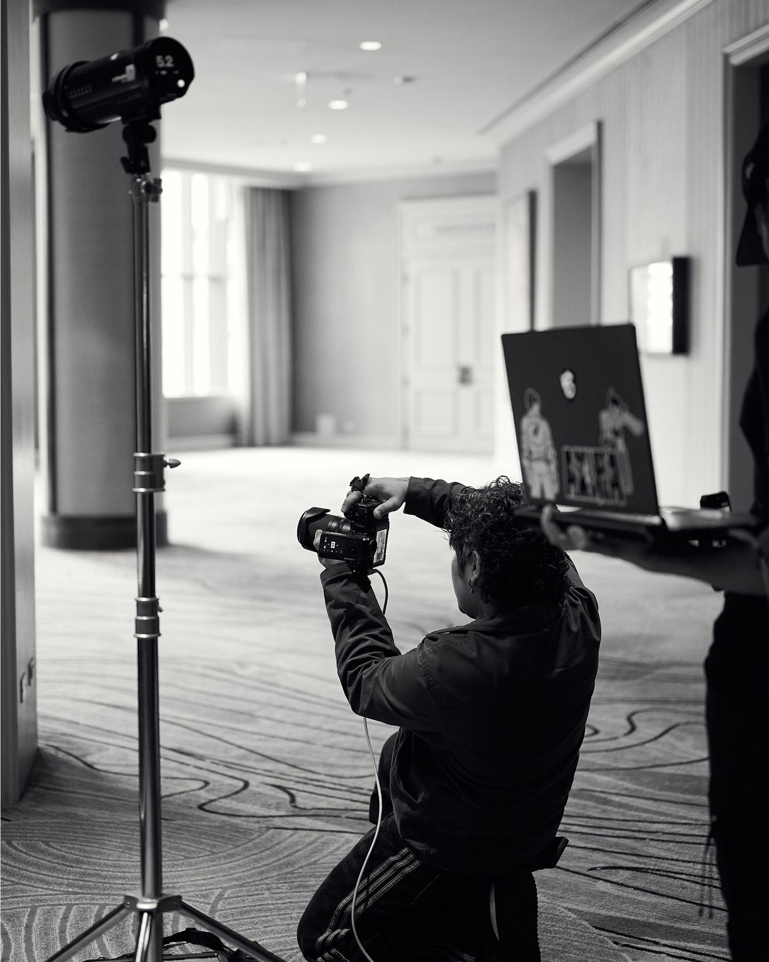 Black and white photo of photographer kneeling with camera on a tripod in an elegant hotel ballroom.