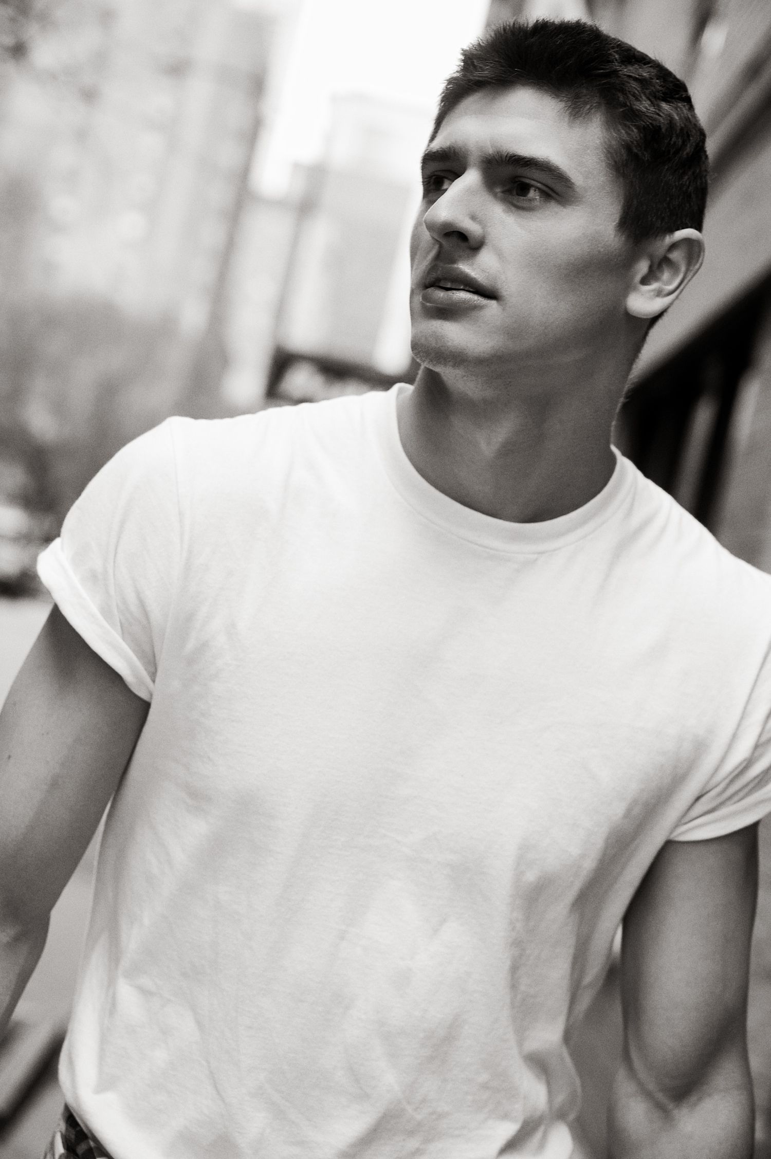 Young man in white t-shirt posing outdoors on urban street in black and white photo.