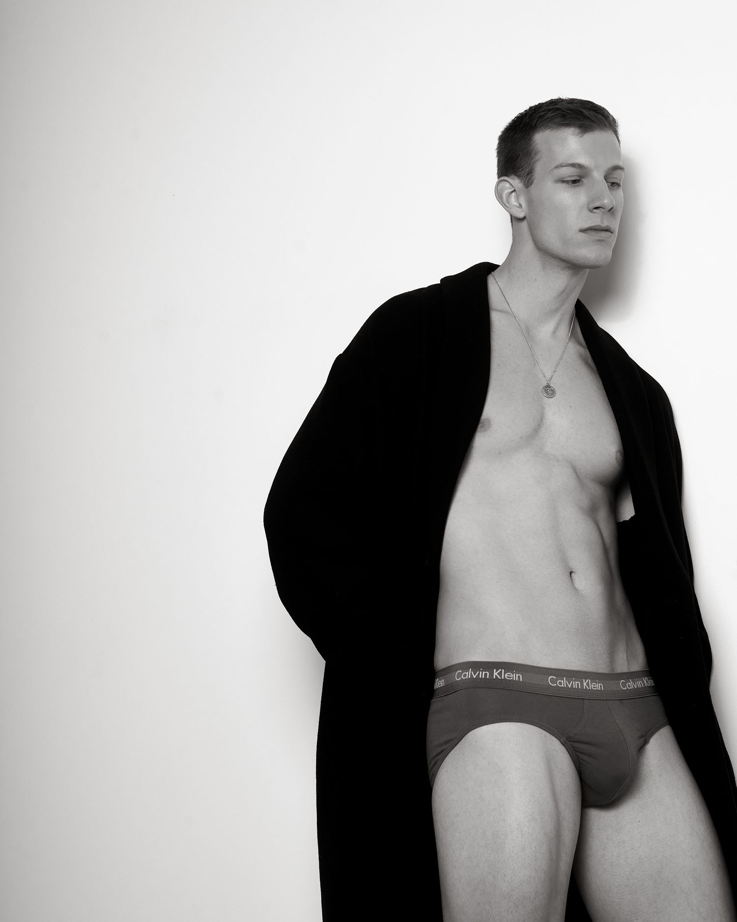 Man in Calvin Klein briefs and black robe posing confidently in a black and white fashion photo.