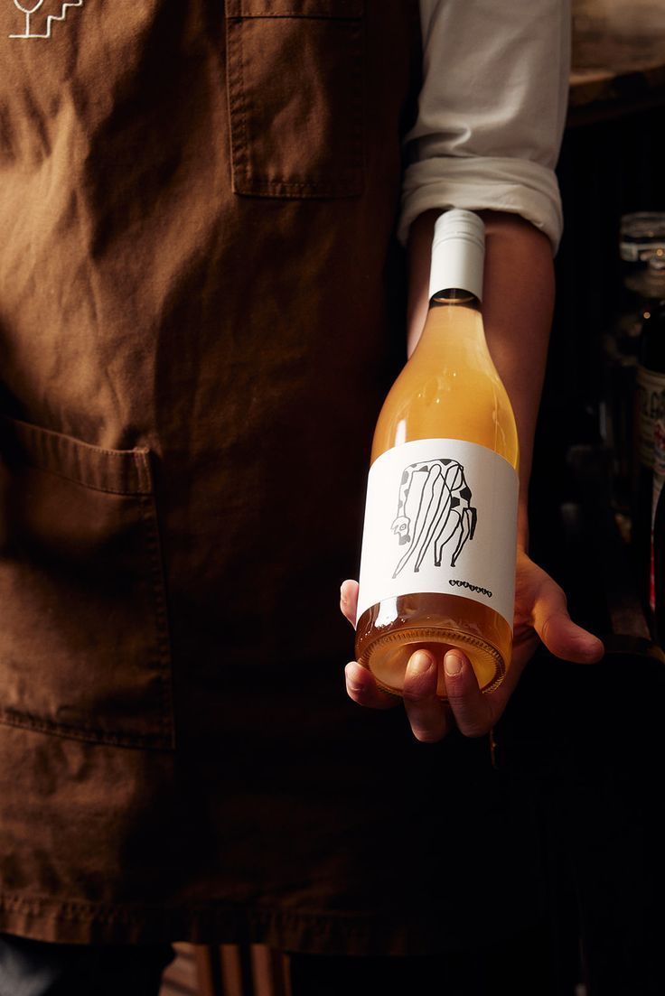 Person in brown apron holding a bottle of orange wine with minimalist bison label design.