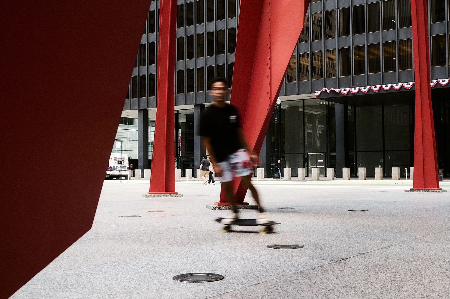 Man riding a skateboard past large red metal sculpture outside a modern office building.