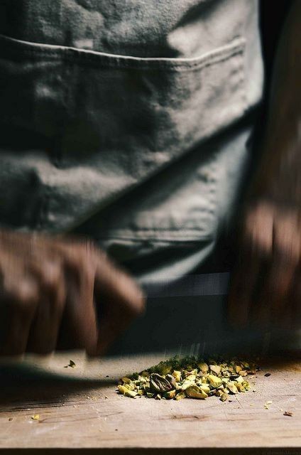 Chef's hands motion-blurred while chopping fresh herbs on a wooden cutting board, wearing a dark apron.