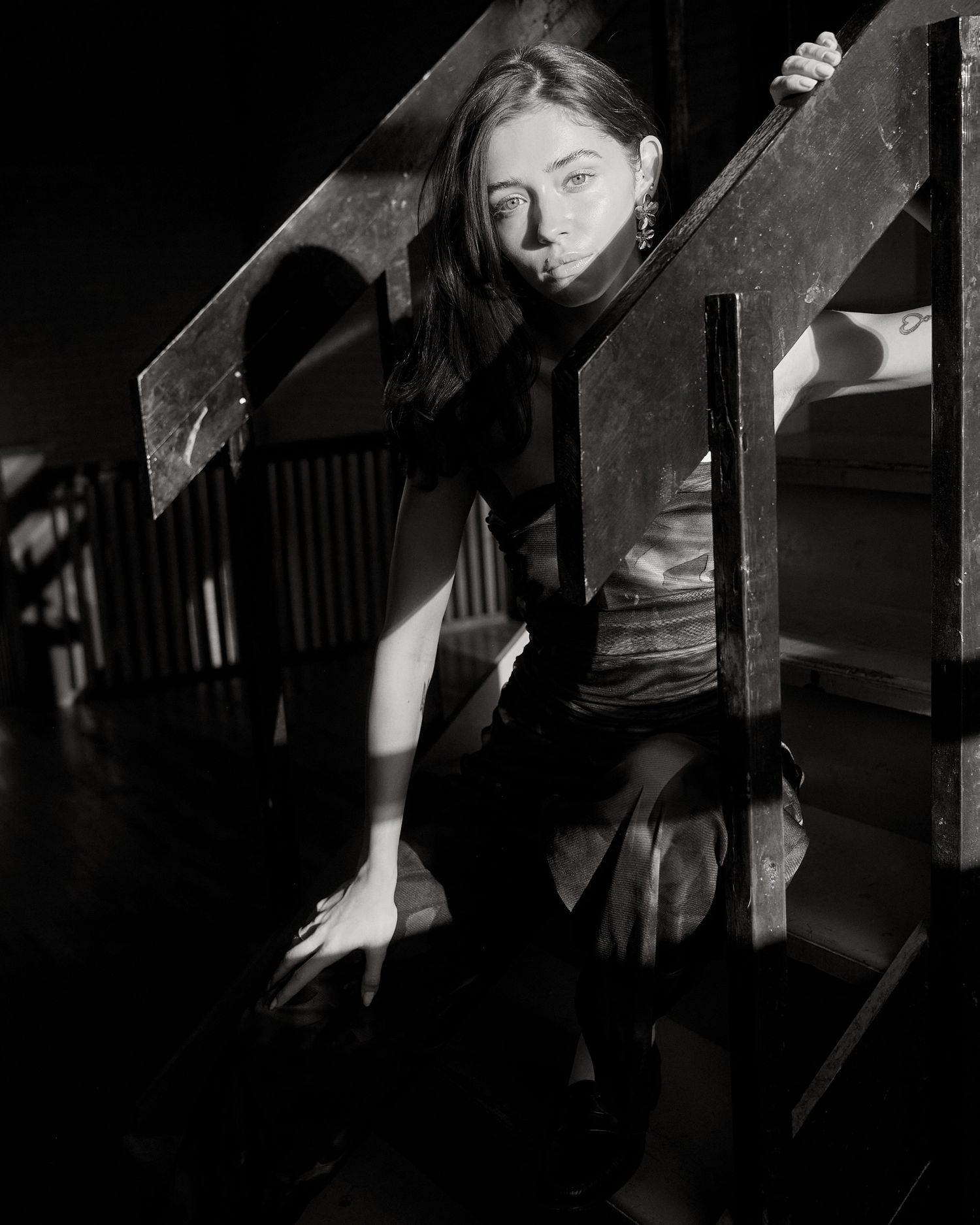 Black and white dramatic photo of a young woman posing between wooden boards in dark lighting.