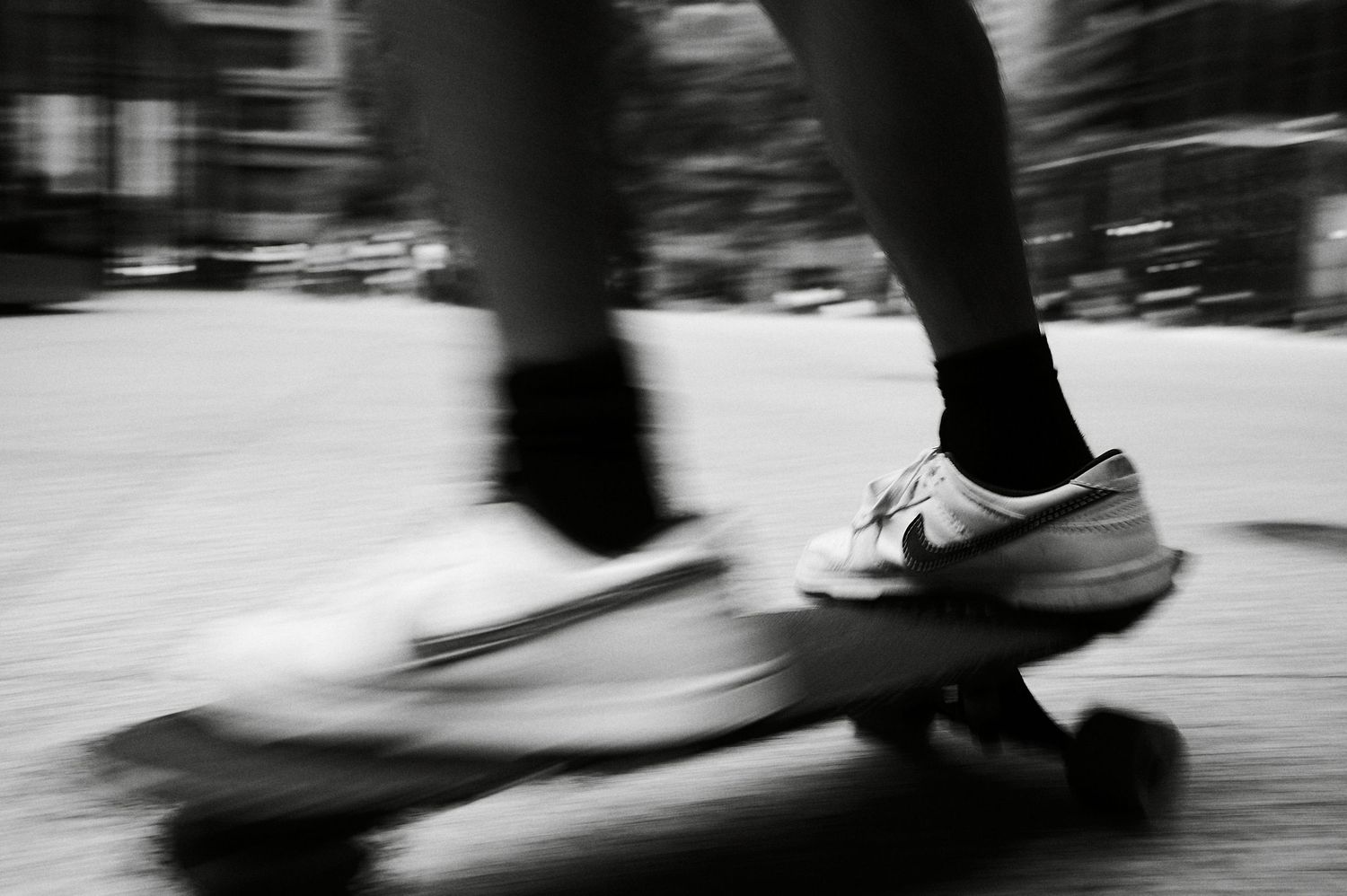Black and white motion blur photo of a skateboarder wearing Nike sneakers and black socks riding a skateboard.