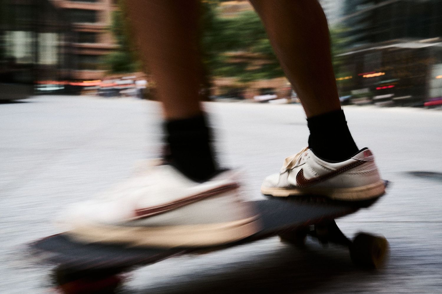 Close-up of a skateboarder wearing Nike sneakers and black socks riding a skateboard at high speed on a city street.