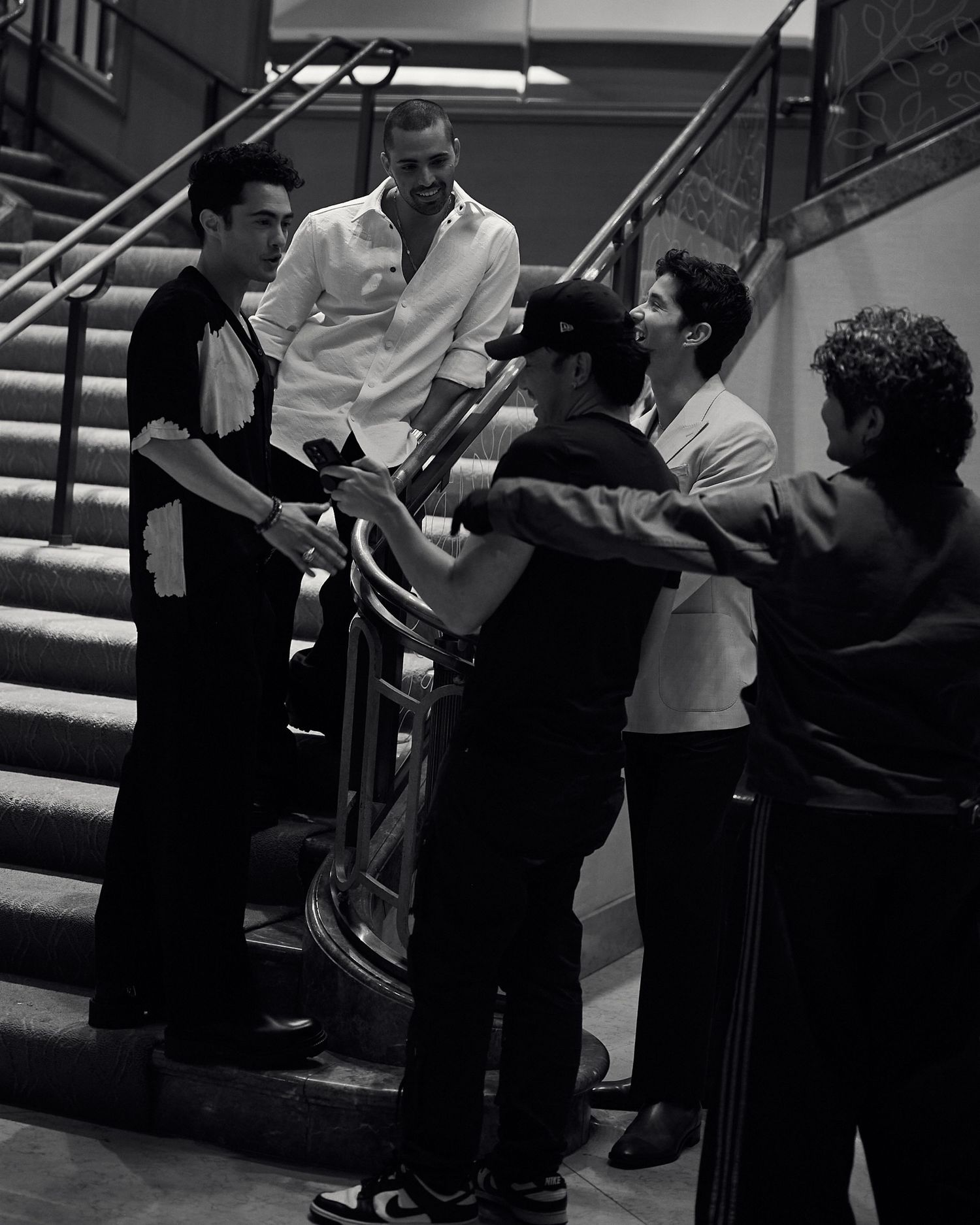 Black and white photo of a group of men conversing on a staircase in a elegant building.
