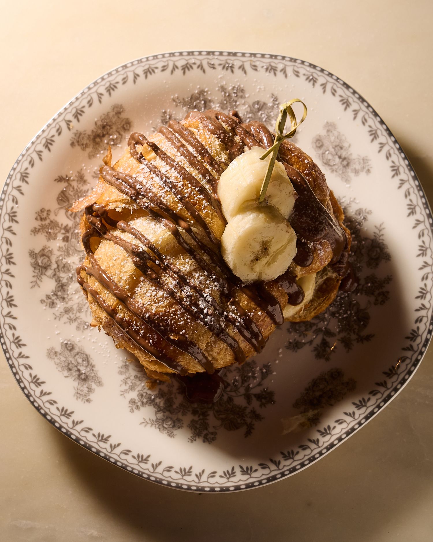 Overhead view of chocolate-drizzled pancakes topped with banana slices on a floral porcelain plate.