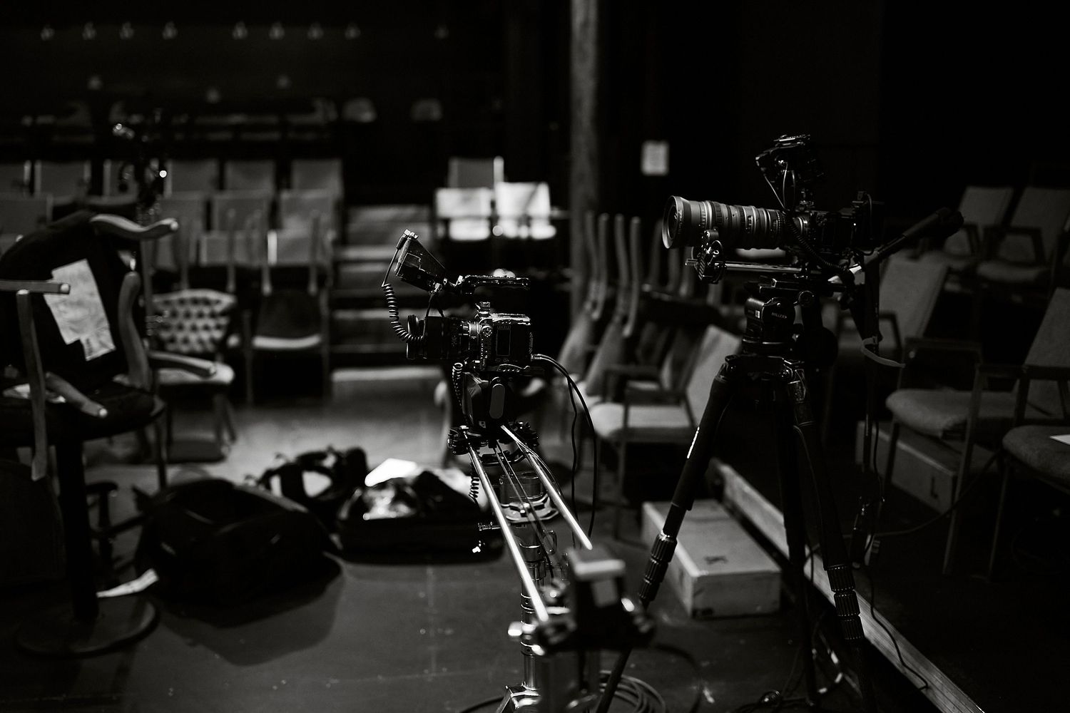 Black and white photo of professional film cameras on tripods set up in a dark theater or studio space.