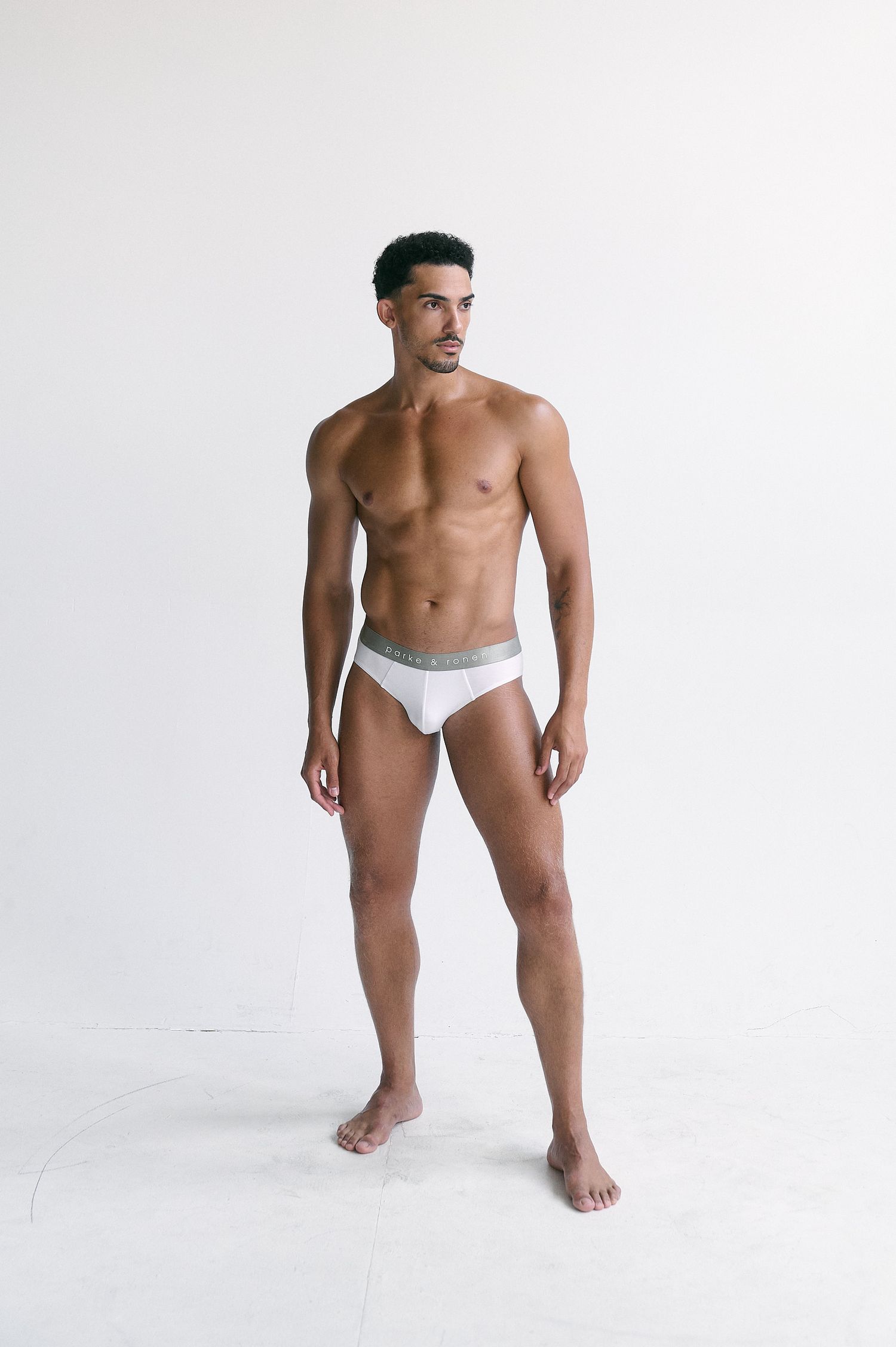 Athletic man posing in white briefs underwear against a clean white studio background.