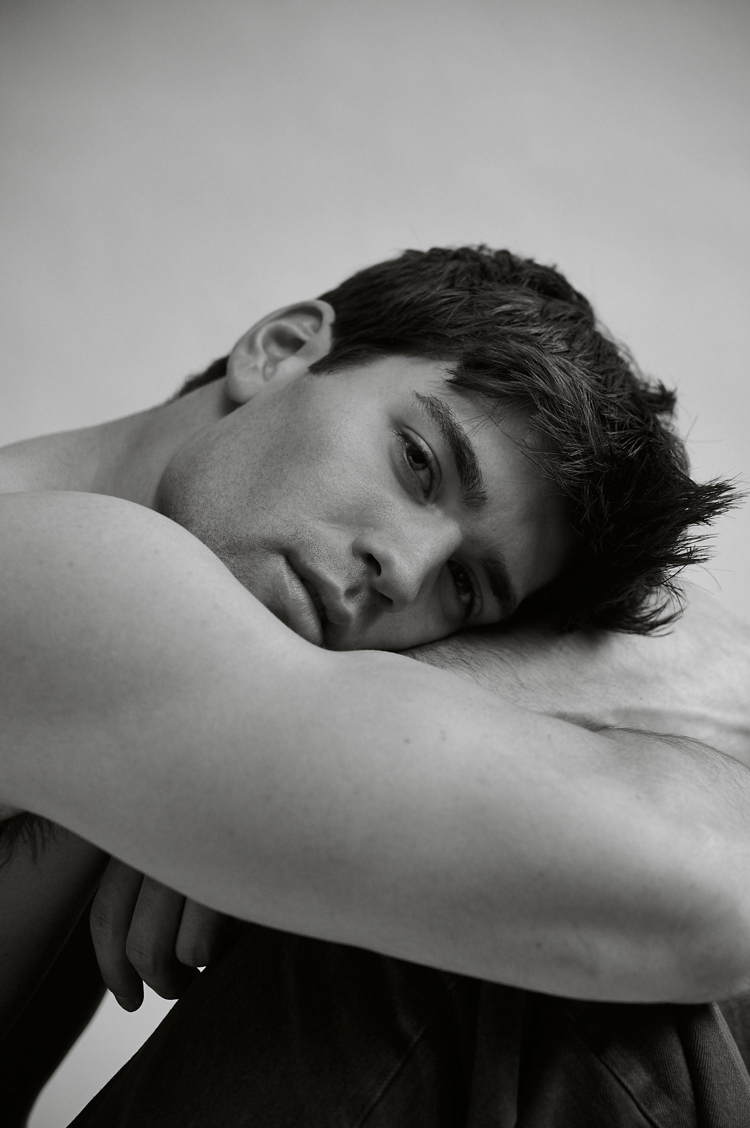 Black and white portrait of a shirtless young man resting his chin on his arms, looking contemplative.