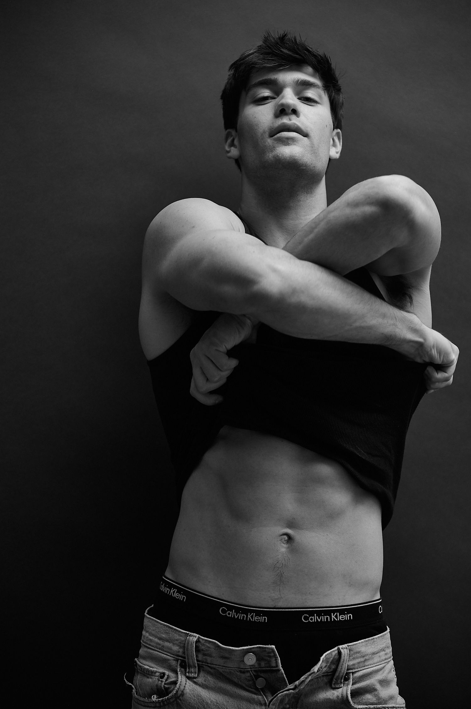 Muscular young man in black crop top and Calvin Klein underwear posing in black and white photo.