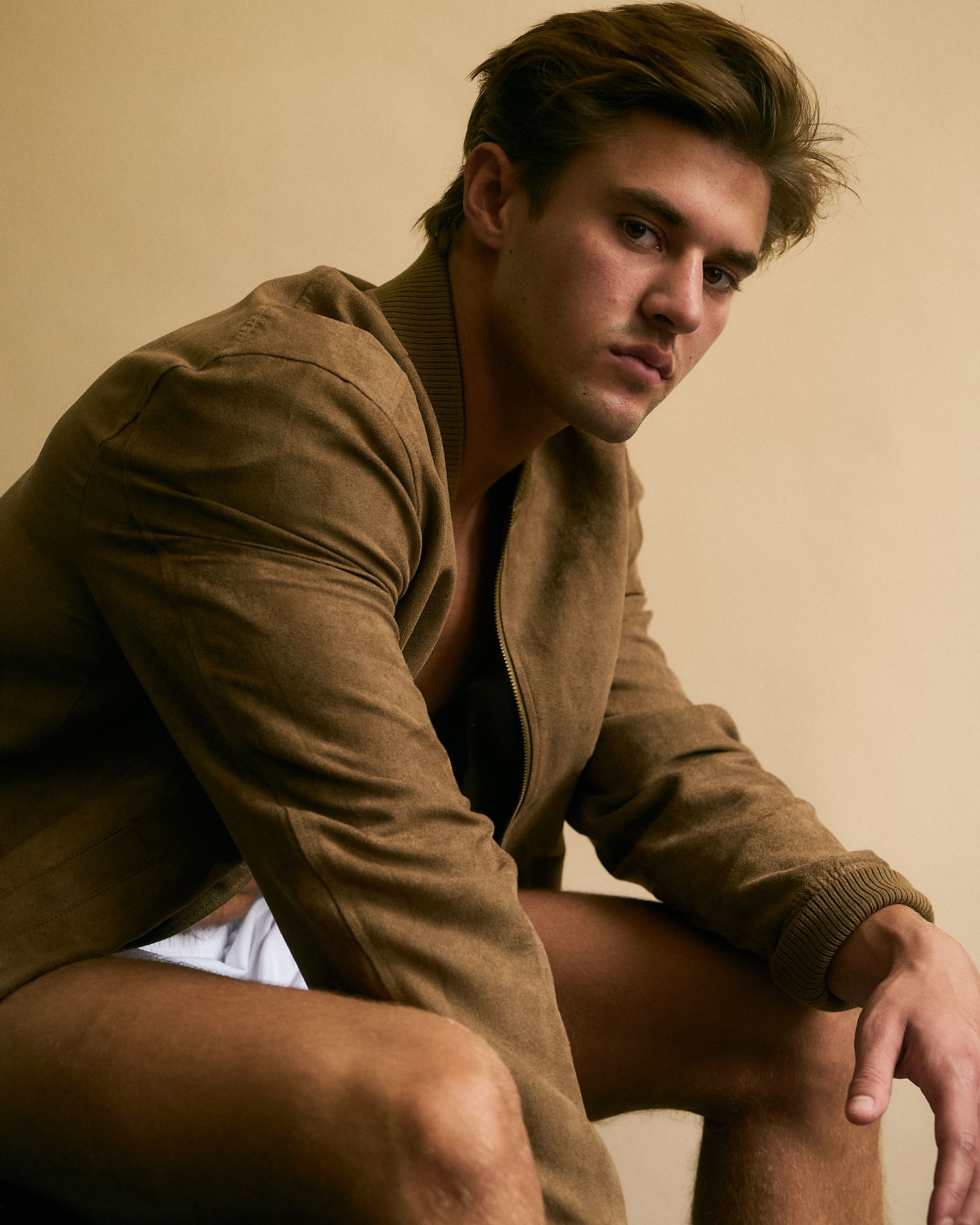 Young man in brown suede jacket and white shorts posing confidently in a stylish fashion editorial photo.