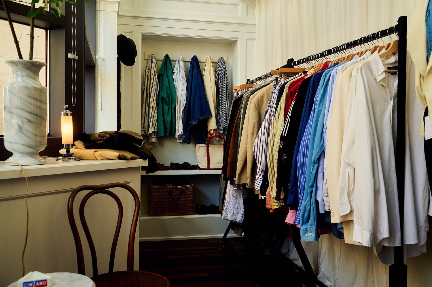 Clothing rack filled with colorful shirts and garments in a boutique shop with wooden furniture and warm lighting.