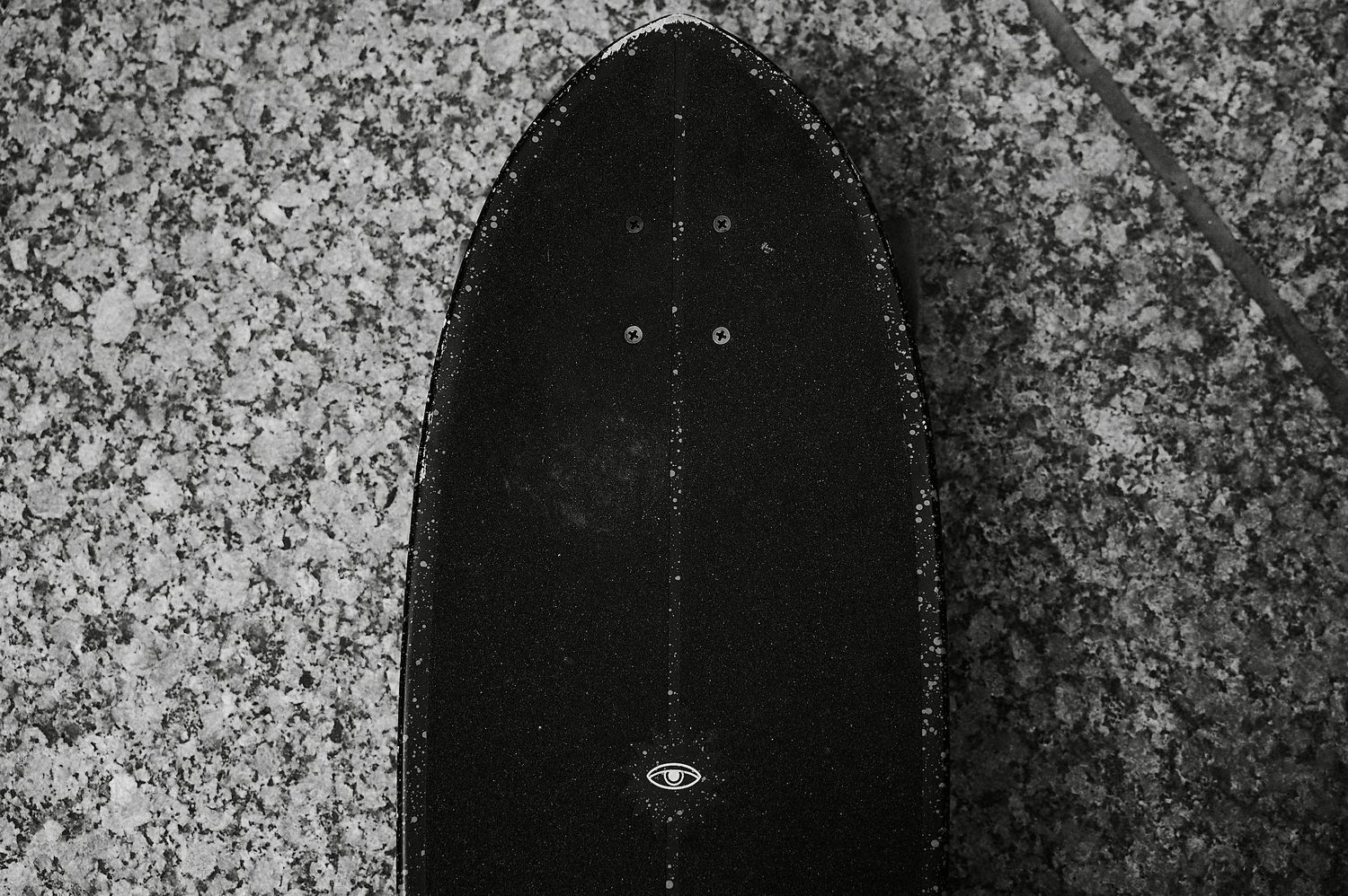 Close-up black and white photo of the bottom of a skateboard deck on a granite surface.