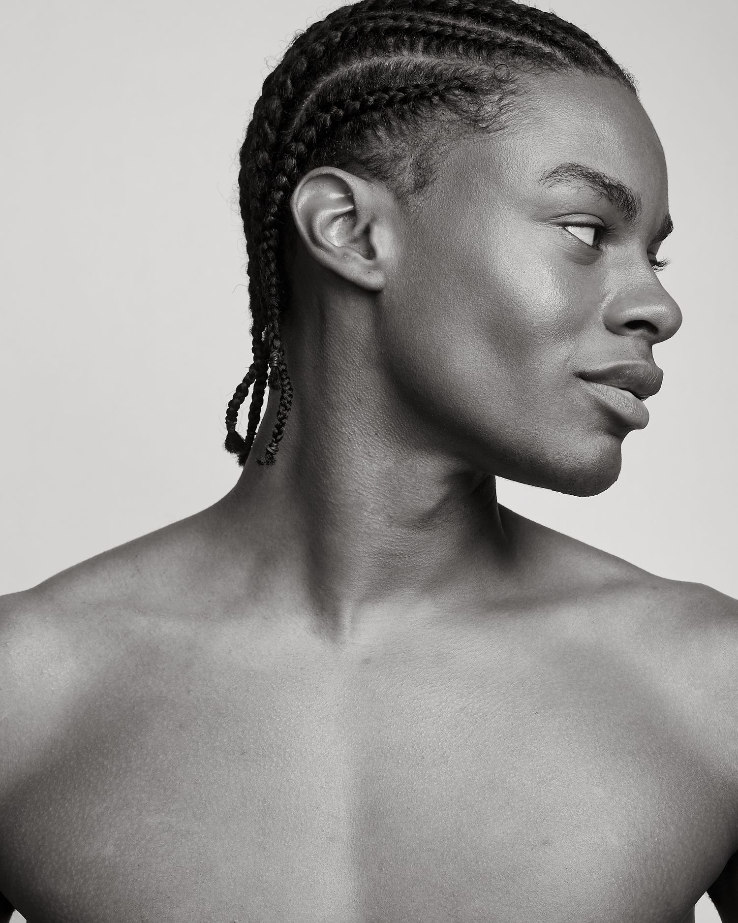 Black and white profile portrait of a shirtless model with braided hair looking to the side.