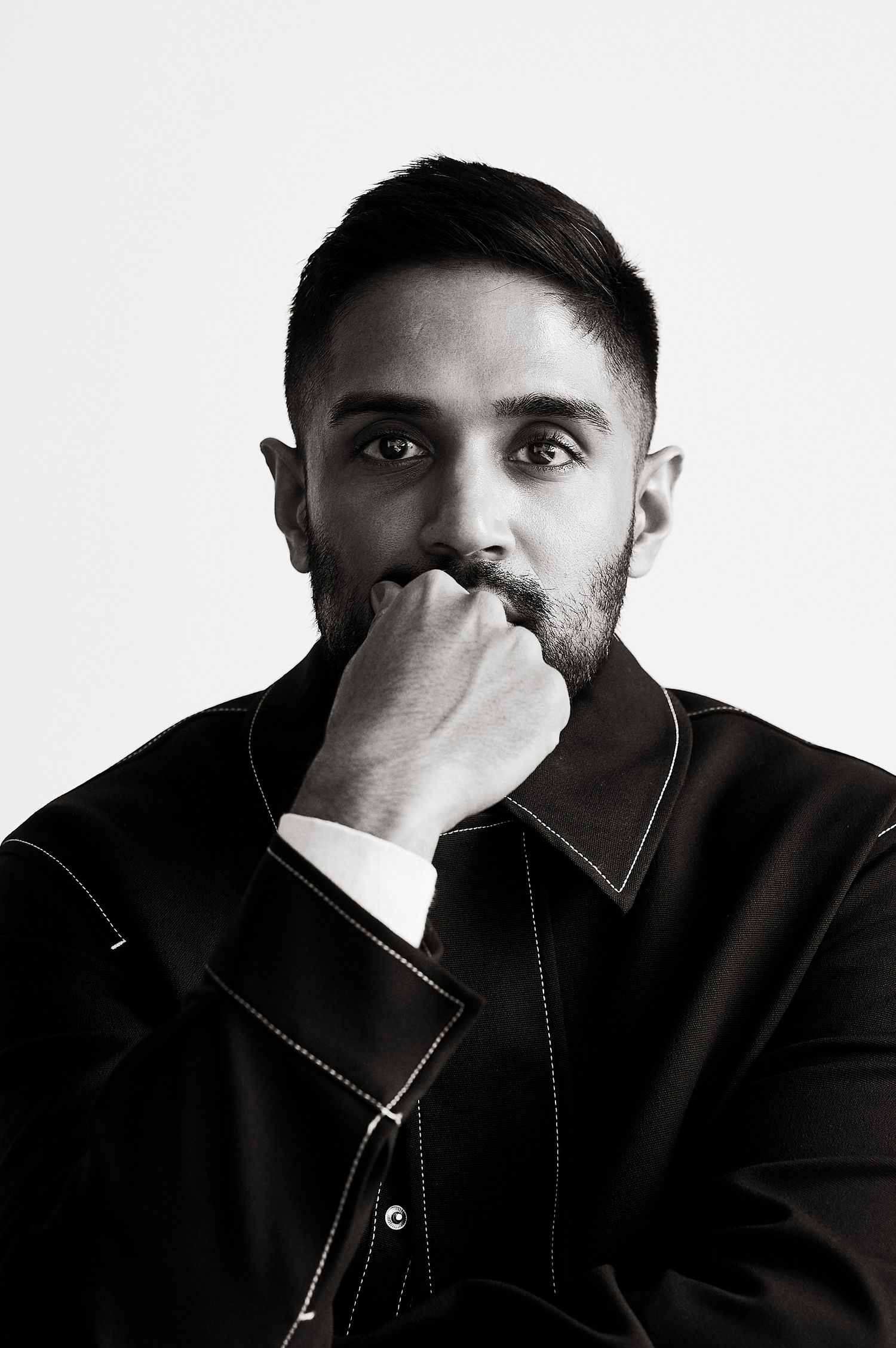 Black and white portrait of a bearded man in a black jacket with hand raised to his mouth.