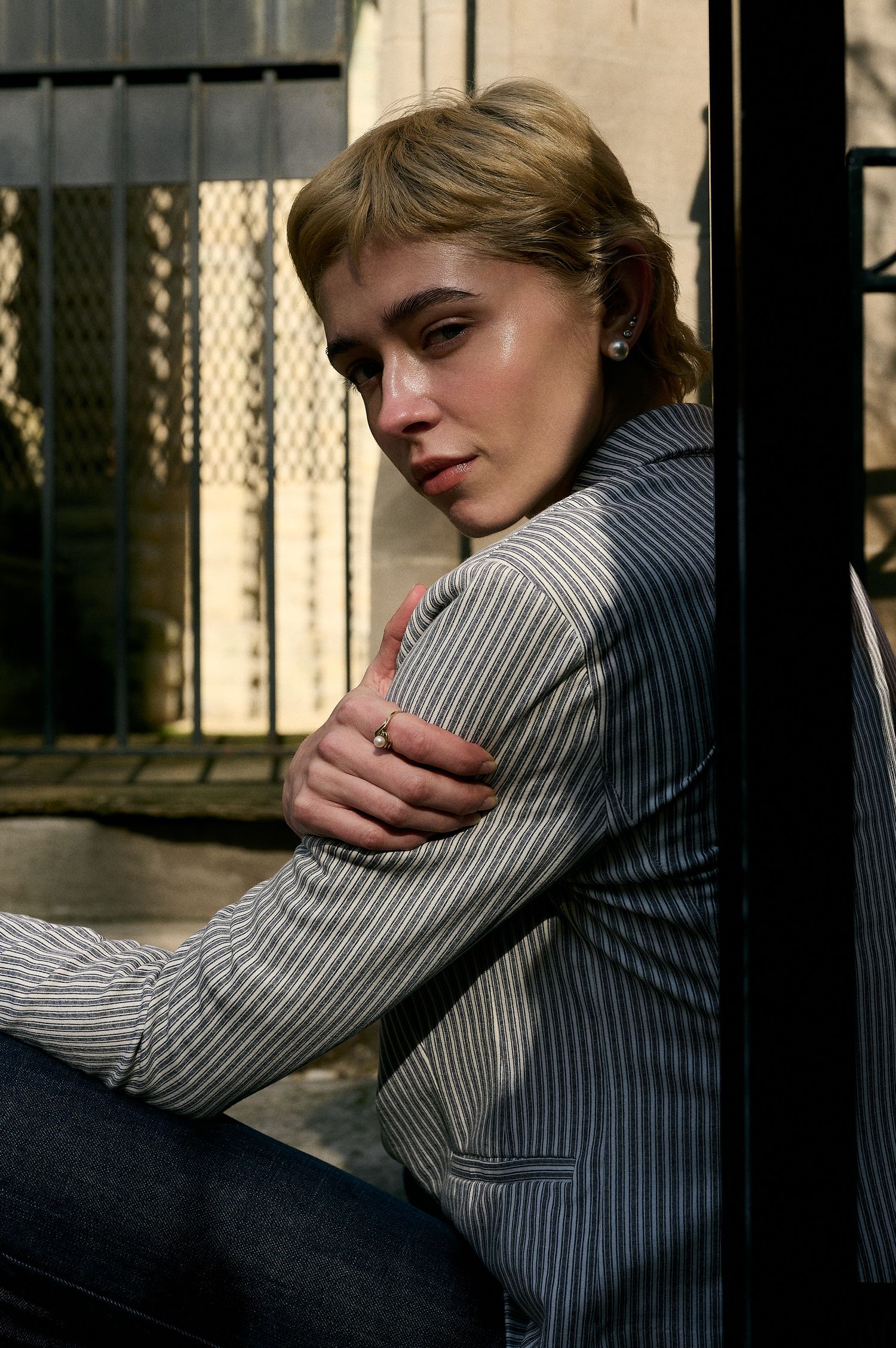 Young blonde woman in pinstripe blazer sits with arms crossed in contemplative color outdoor portrait photo.