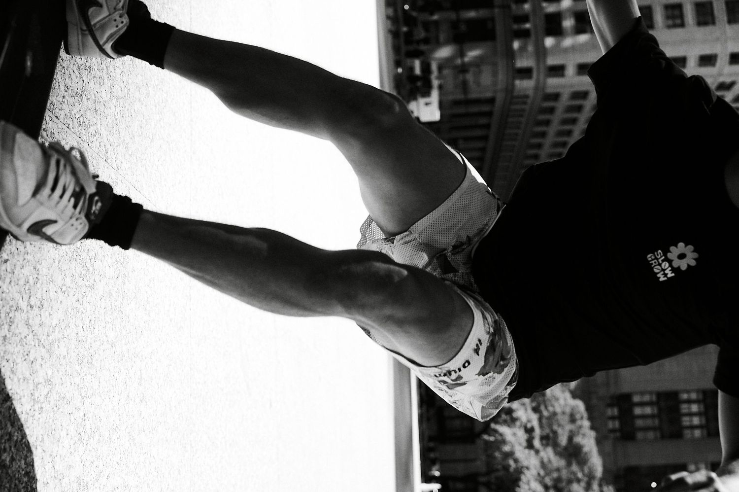 Black and white close-up of a skateboarder's legs and shoes against an urban wall.