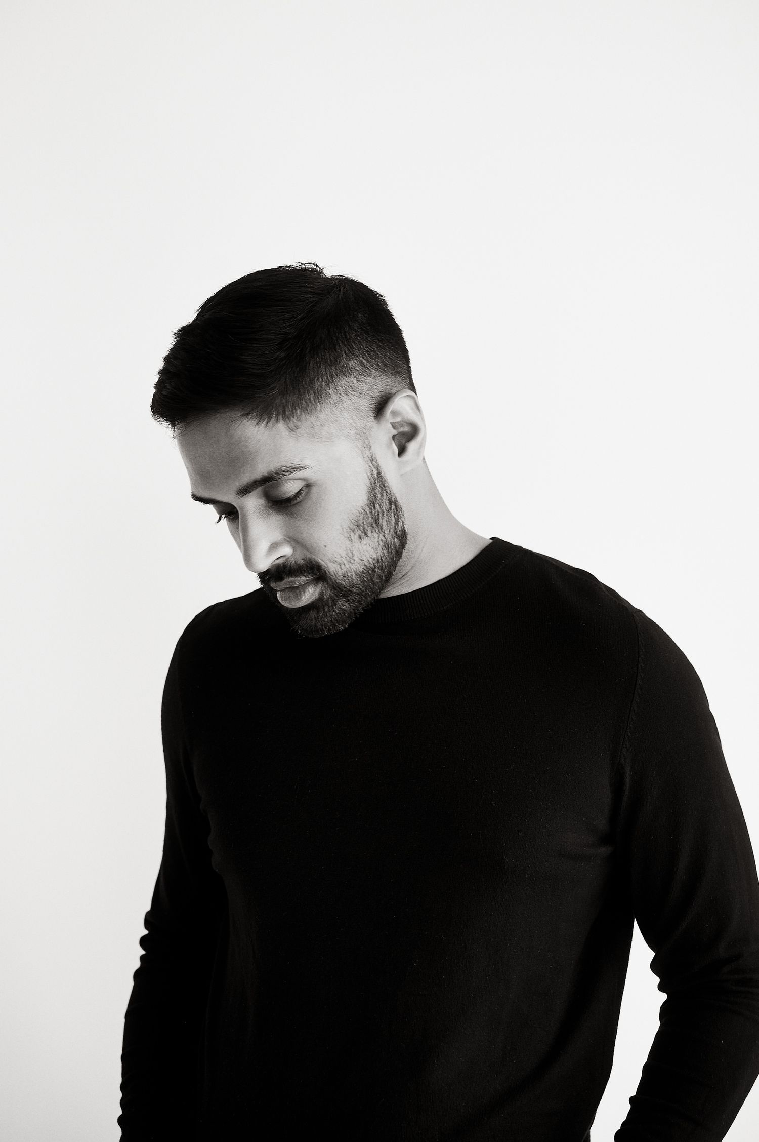 Black and white portrait of a bearded man in a black sweater looking downward thoughtfully.