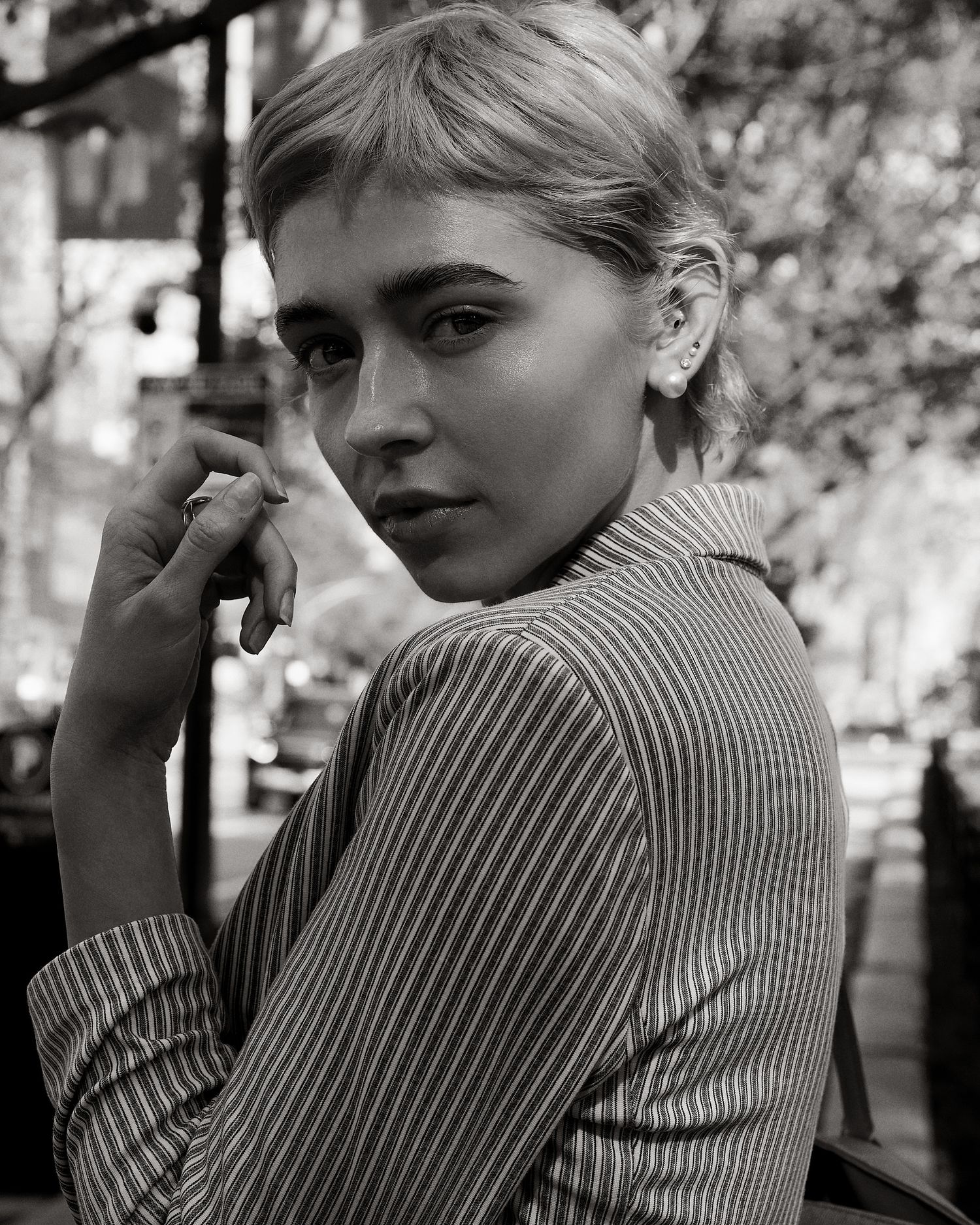 Black and white portrait of a short-haired blonde woman in a striped shirt outdoors.