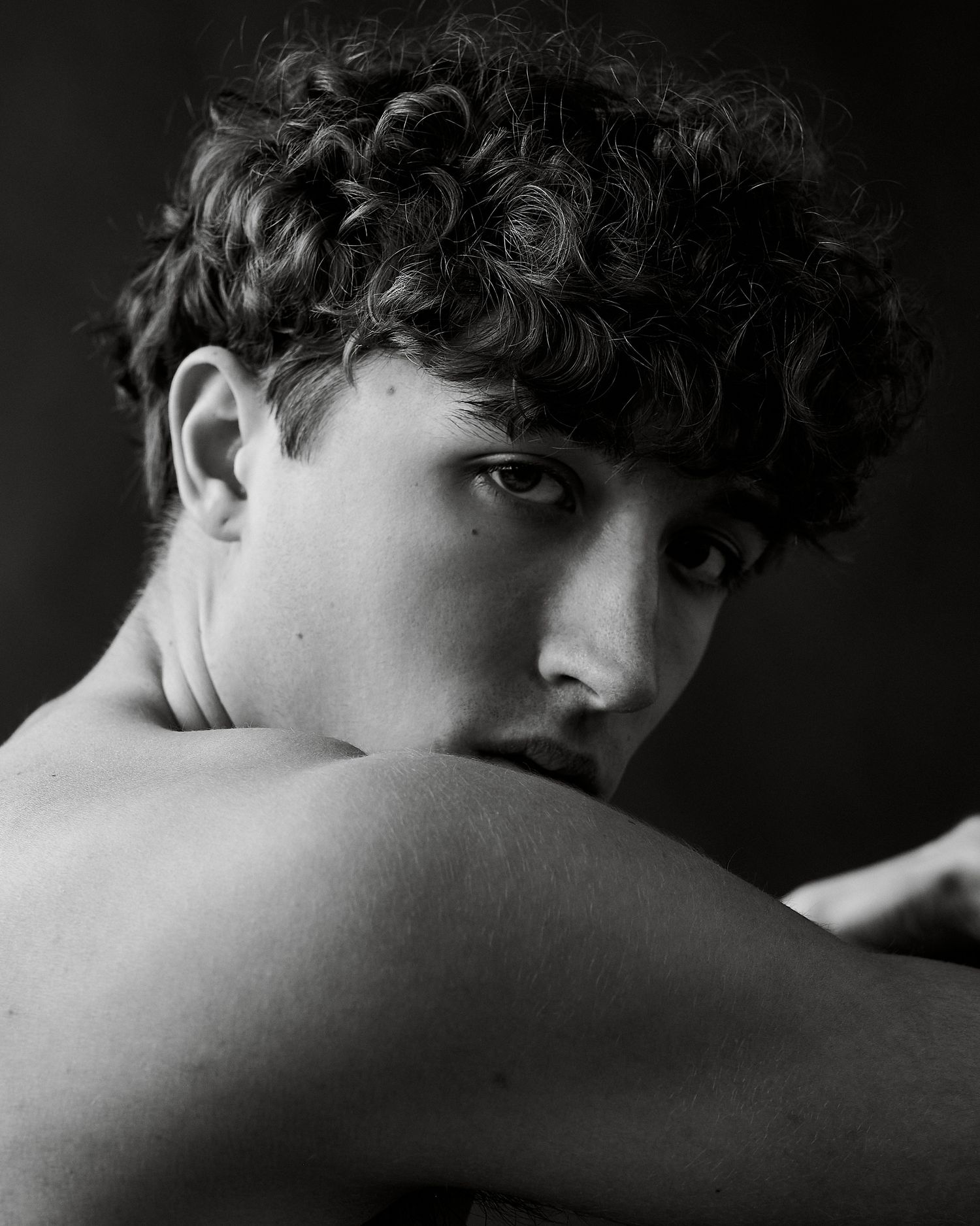 Black and white close-up portrait of a curly-haired young man looking over his shoulder.