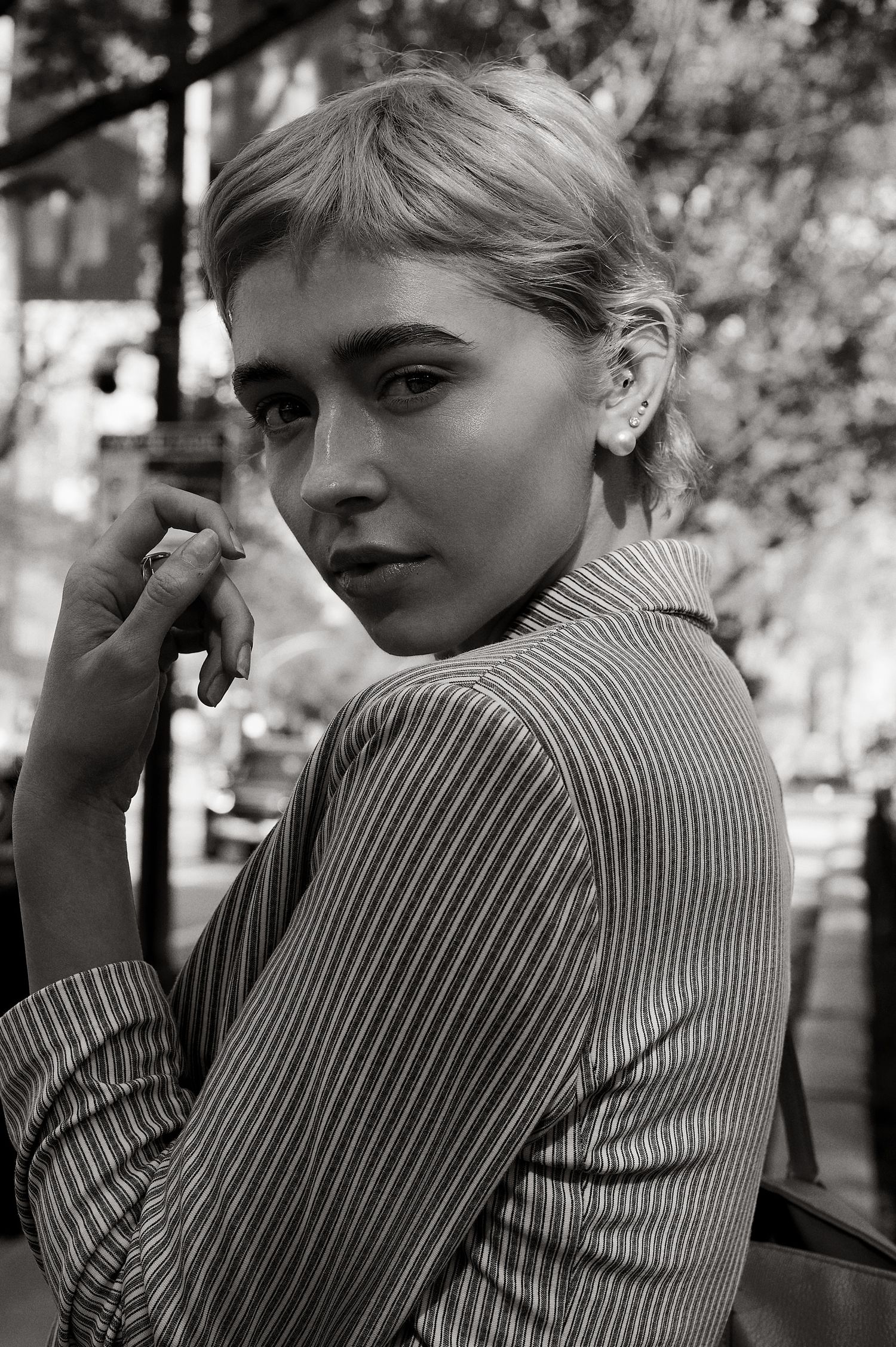 Young blonde woman in pinstripe blazer looks intensely at camera in black and white urban outdoor portrait.
