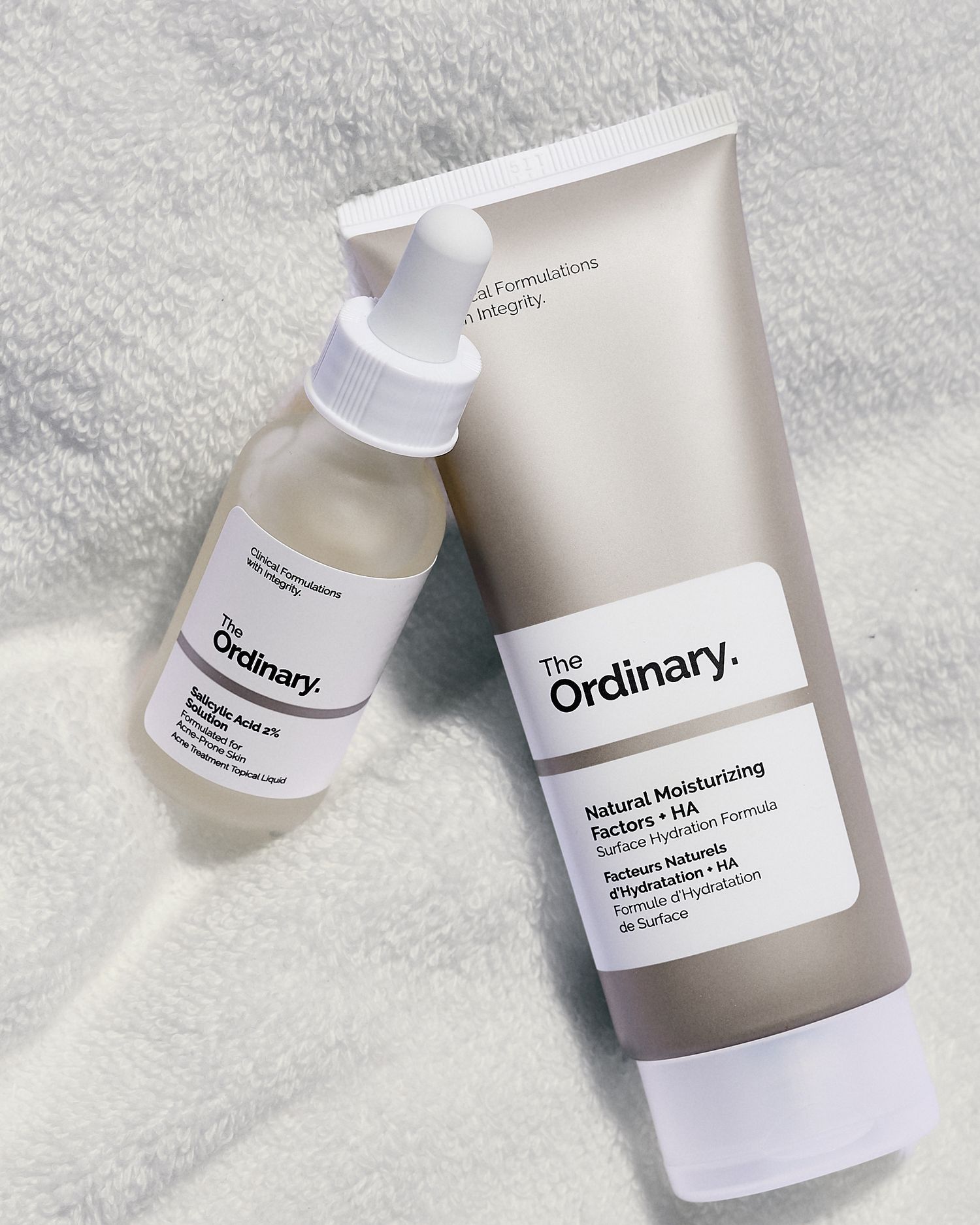 Two The Ordinary skincare products, Natural Moisturizing Factors HA and Salicylic Acid serum, on a white towel.