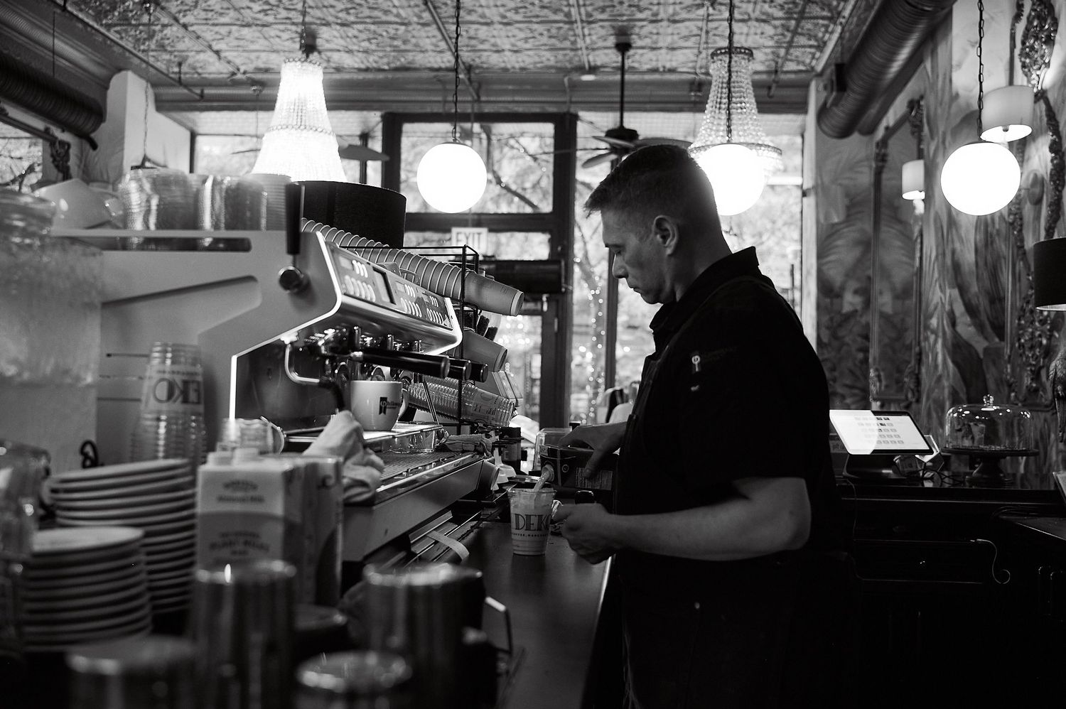 Barista operating espresso machine in a cozy cafe, black and white photo of coffee shop interior.