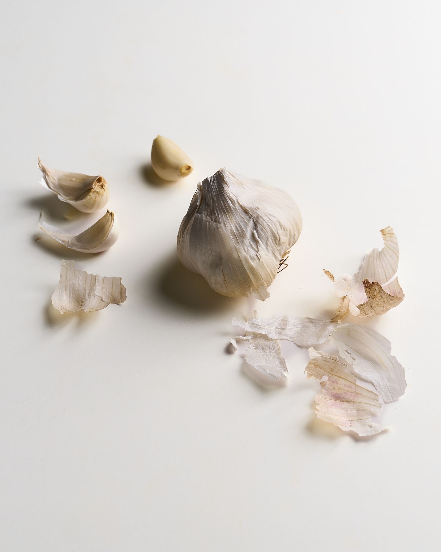 A whole garlic bulb surrounded by loose cloves and papery skin on a white background.