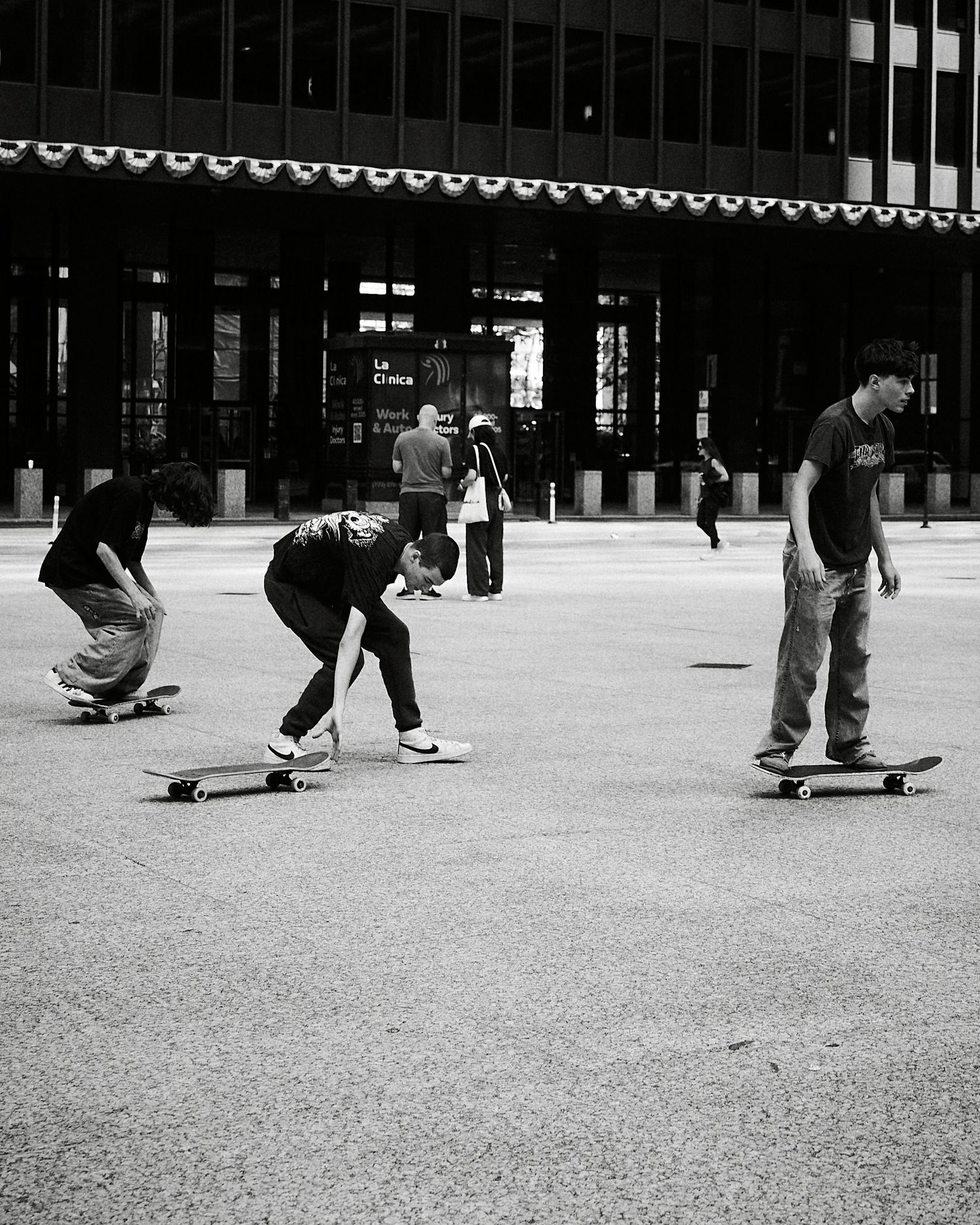 Black and white photo of three skateboarders practicing tricks in an urban plaza.