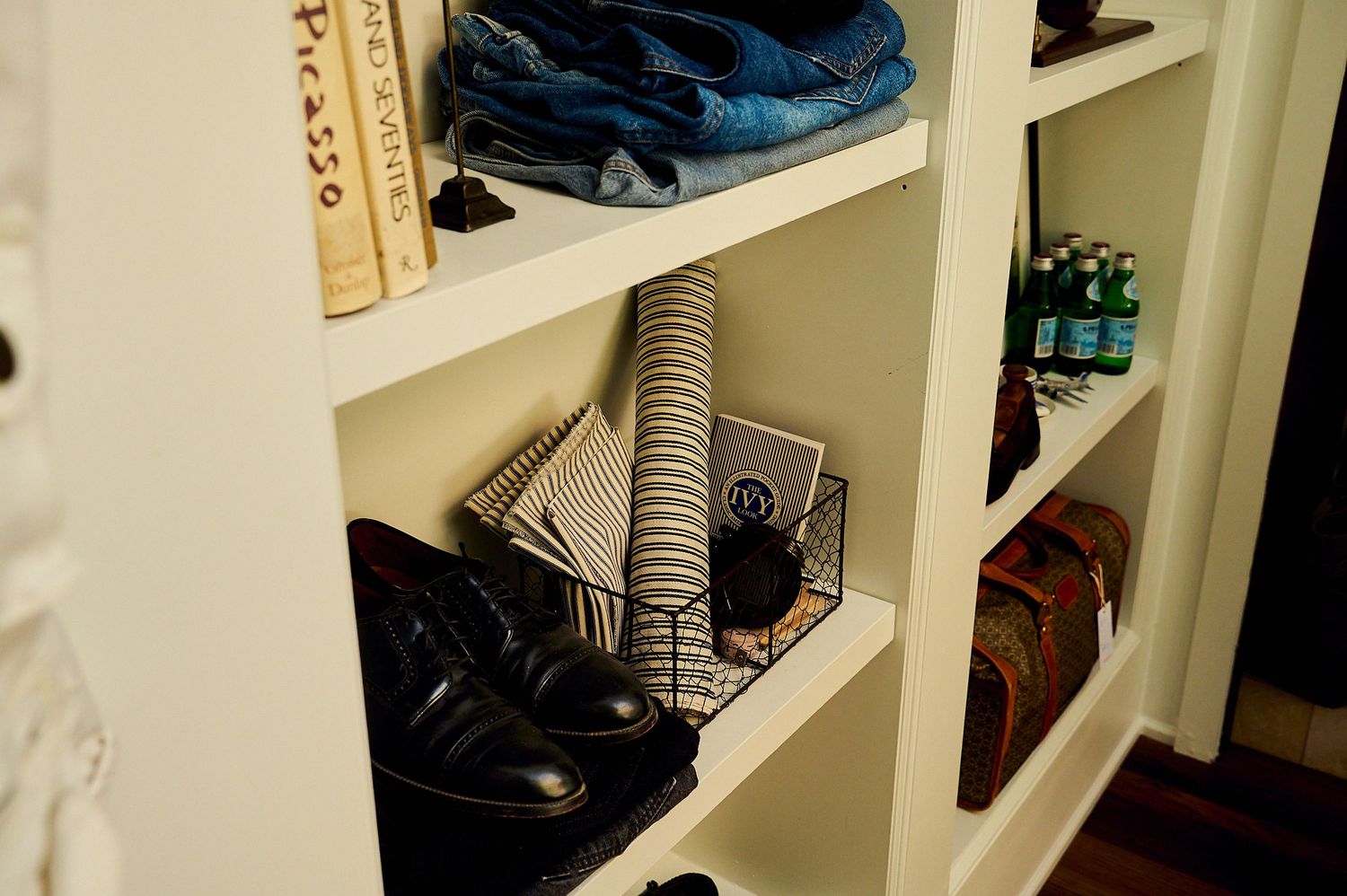 White built-in shelving unit displaying folded clothes, black shoes, books, and accessories in an organized closet.