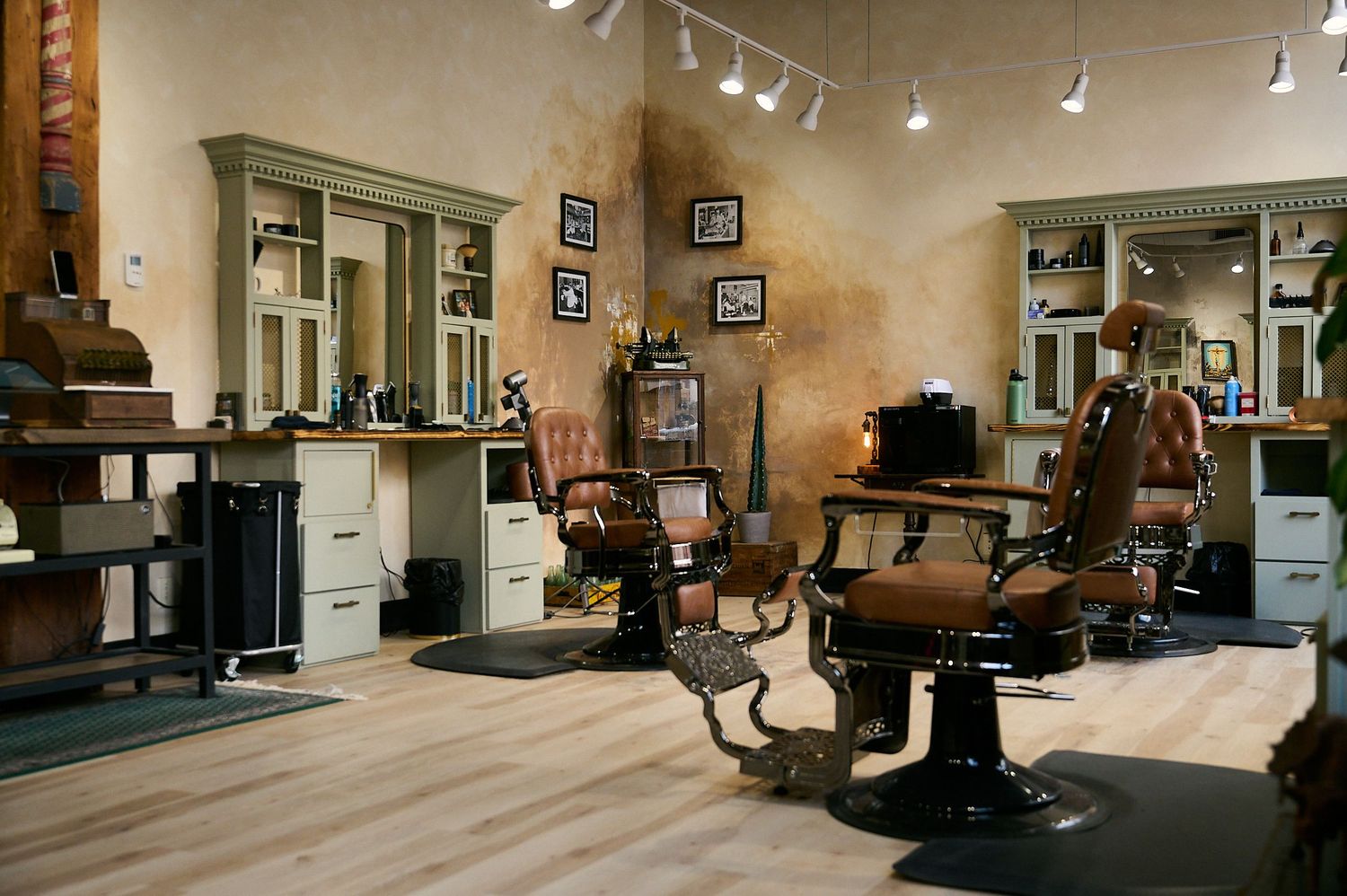 Vintage barber shop interior with classic leather chairs, green cabinets, mirrors, and warm lighting on light wood floors.