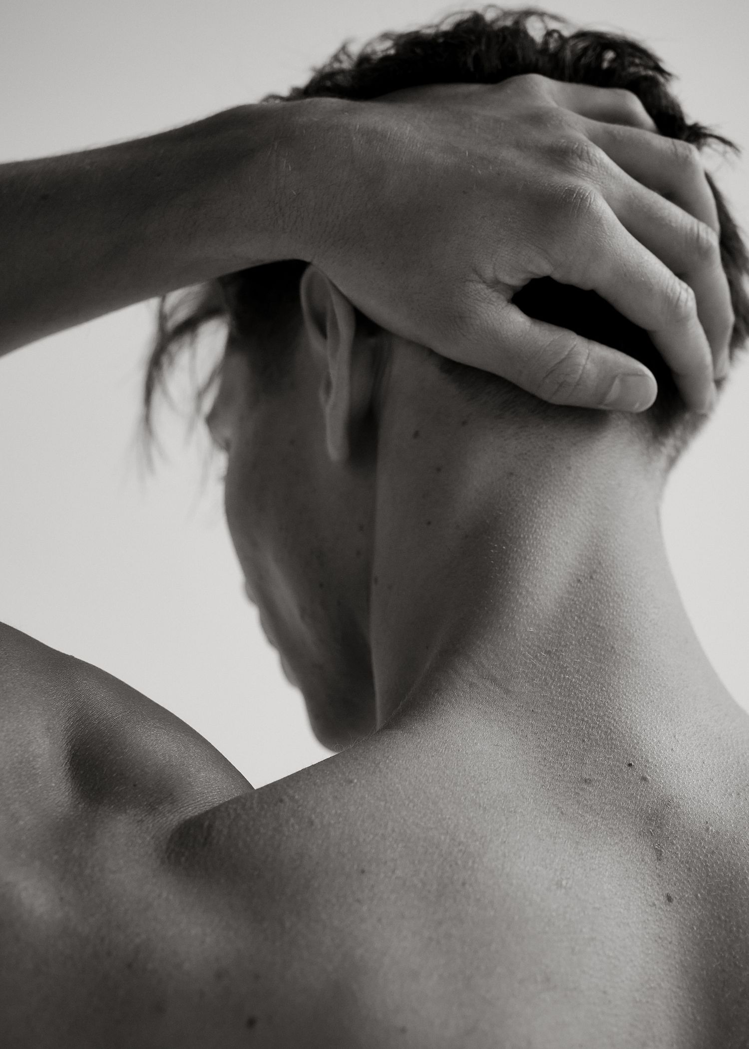 Black and white photo of a person viewed from behind, hand resting on the back of their neck.