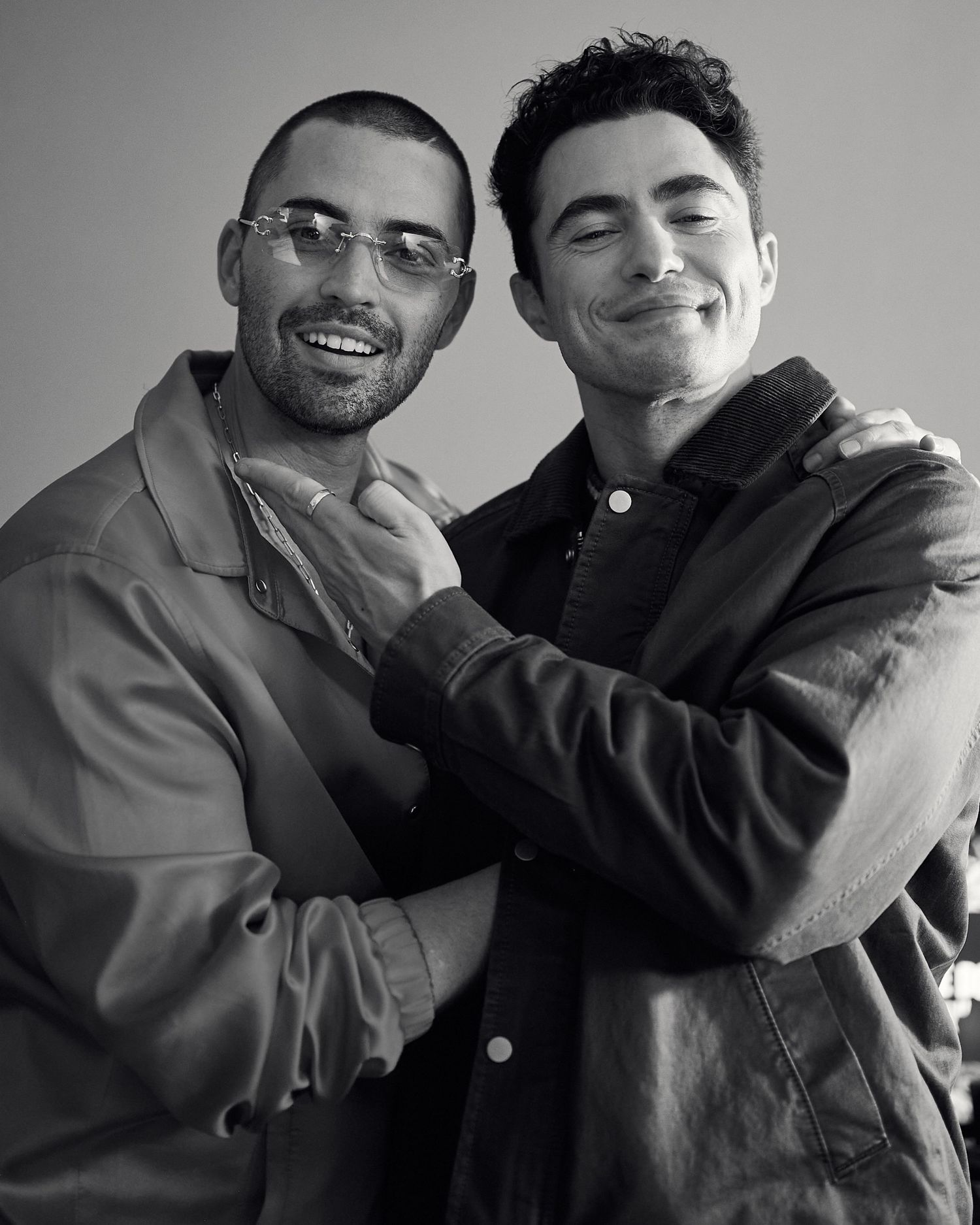 Two smiling men embracing warmly in a black and white portrait photo wearing casual jackets.