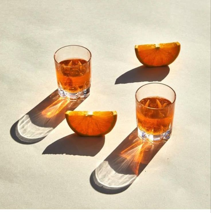 Two shot glasses of amber spirits with fresh orange slices casting long shadows on a bright white surface.