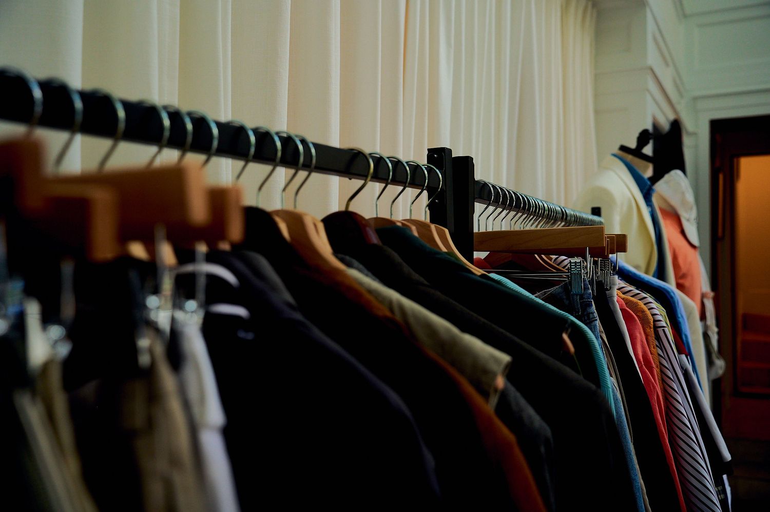 Clothing rack with various jackets and shirts on wooden and black hangers in a well-lit room.