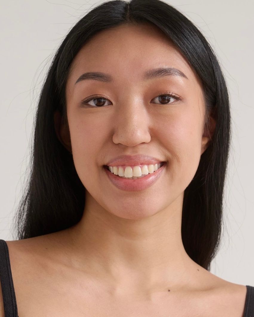 Young woman with long black hair smiling warmly against a white background, wearing a black top.